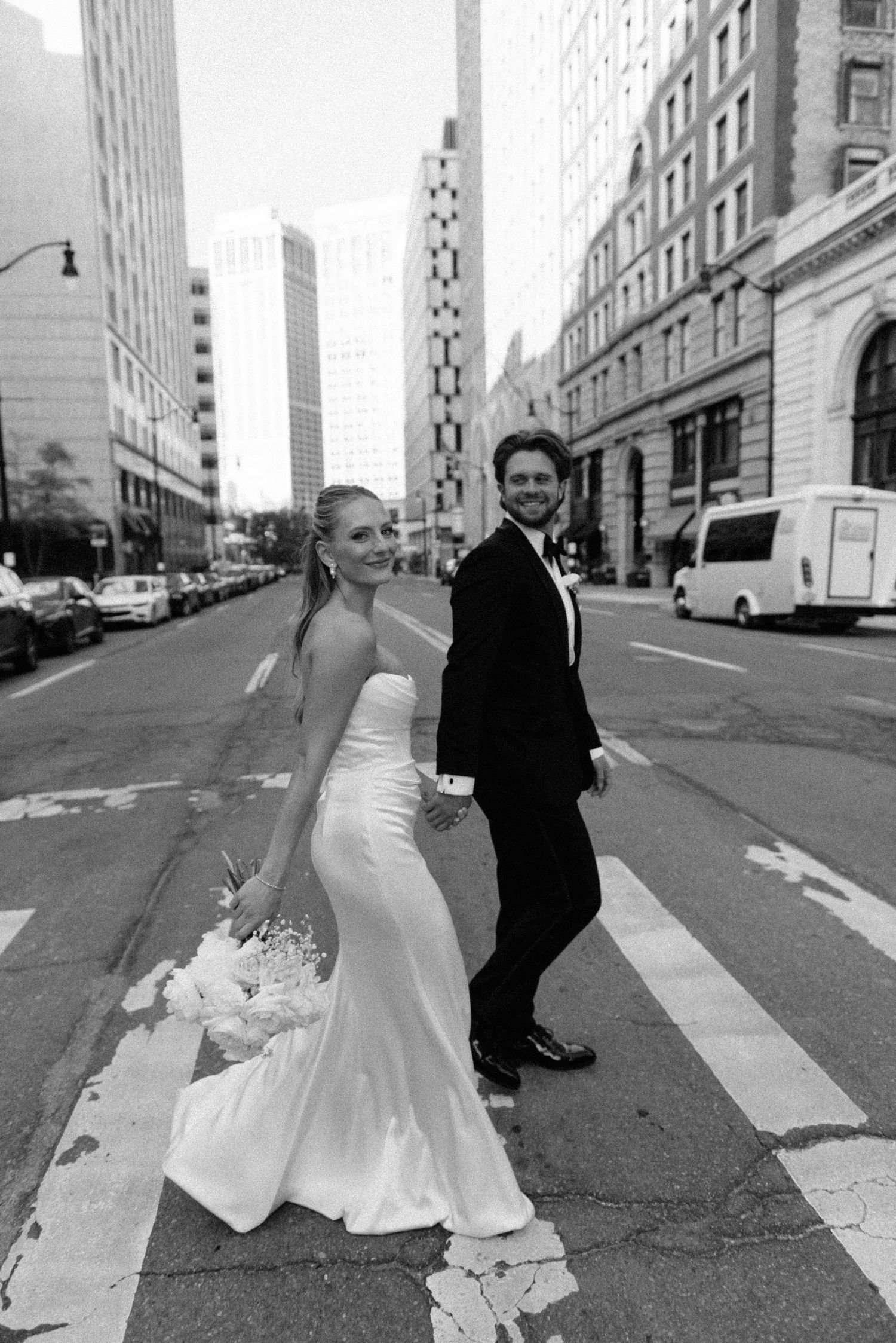 Bride and groom cross city street in black and white wedding portrait.