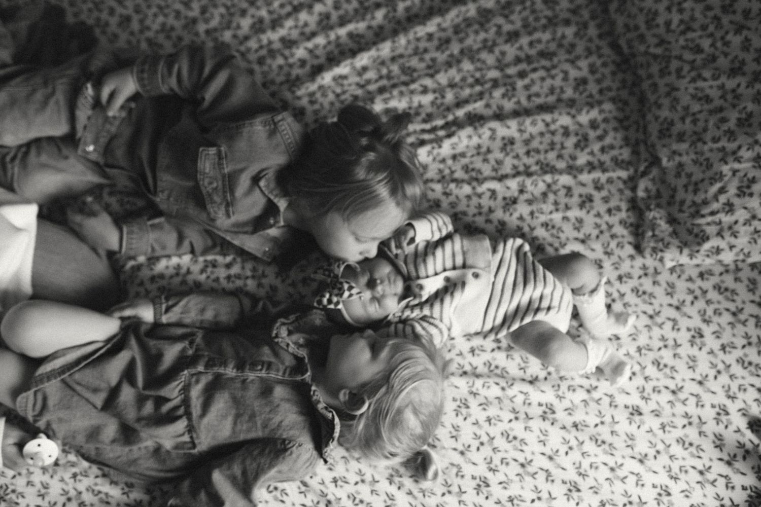 Black and white overhead photo of two young children cuddling together on a floral bed.