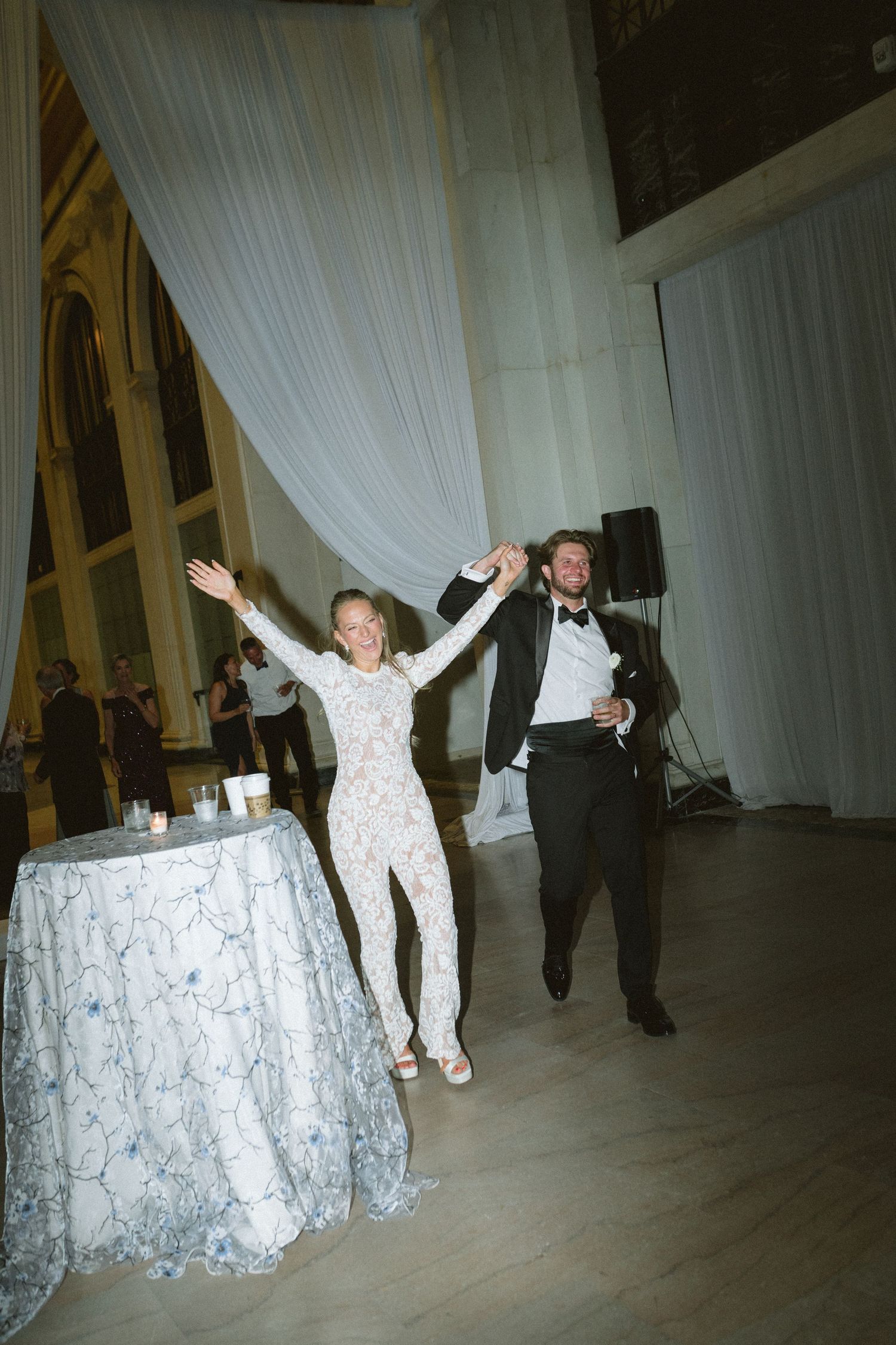 Bride in floral reception dress and groom celebrate joyfully on dance floor.