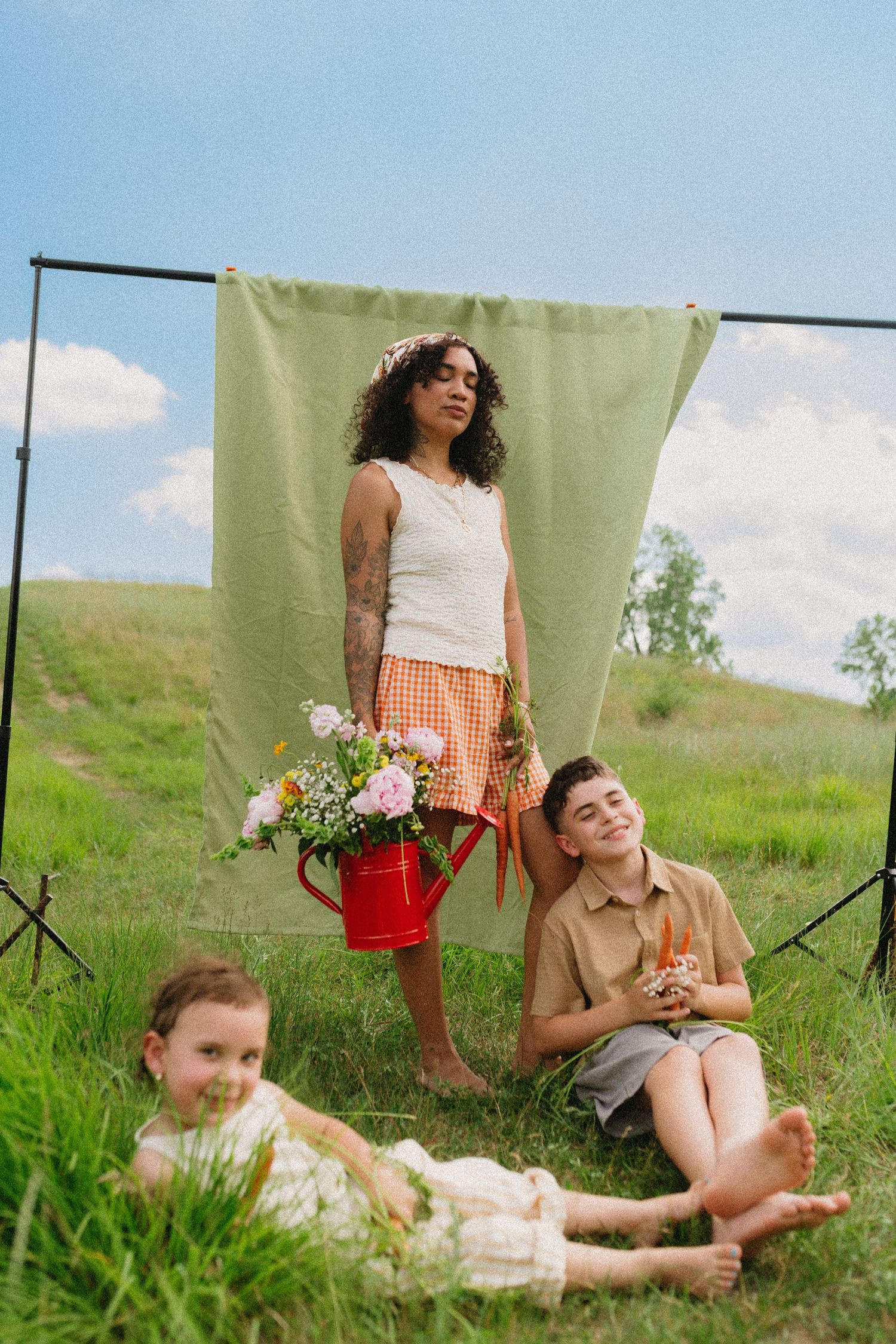 Woman holding flowers stands behind boy and girl posing in front of green backdrop on hillside.