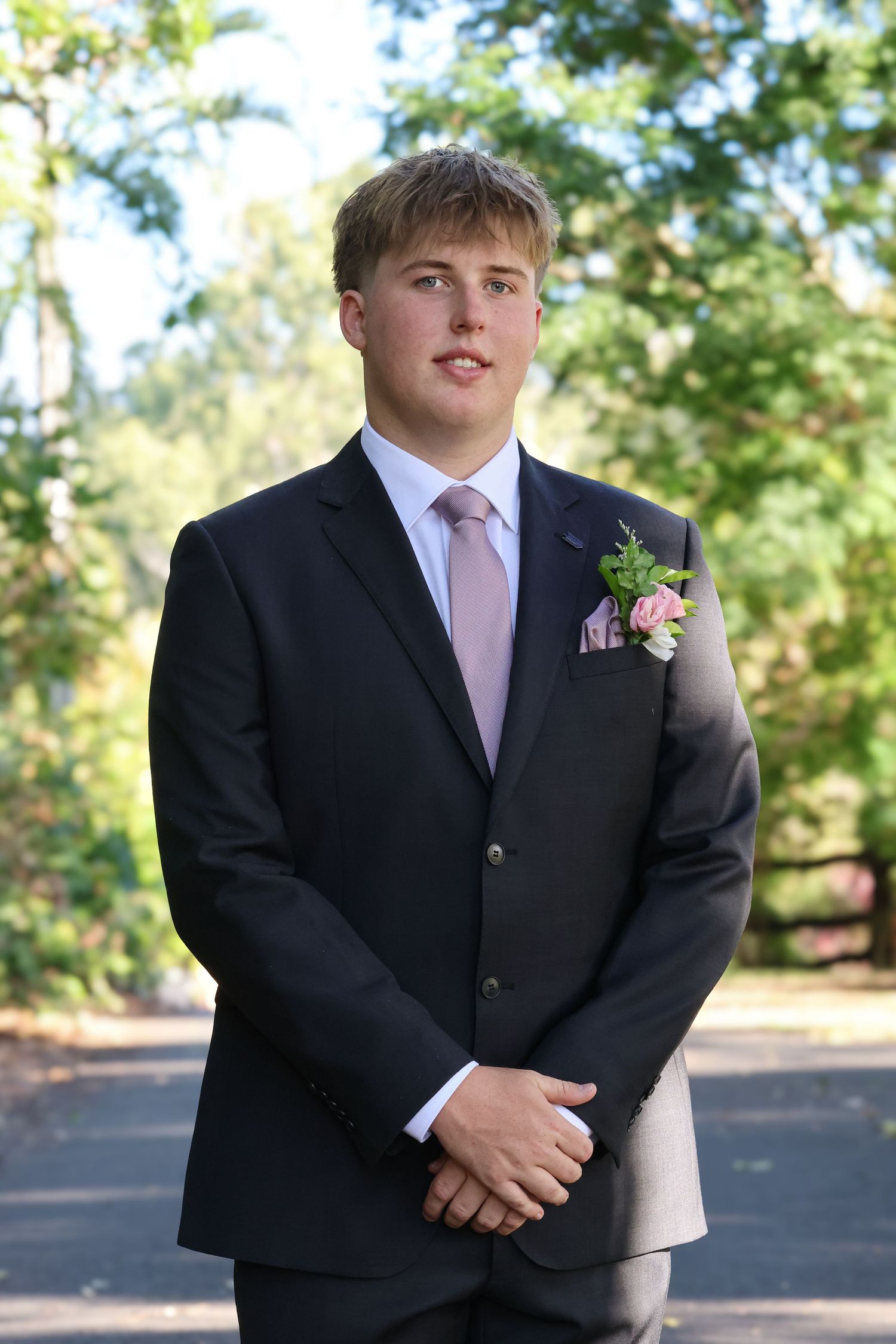 Young man in navy suit with pink boutonniere and tie poses outdoors for prom photo.