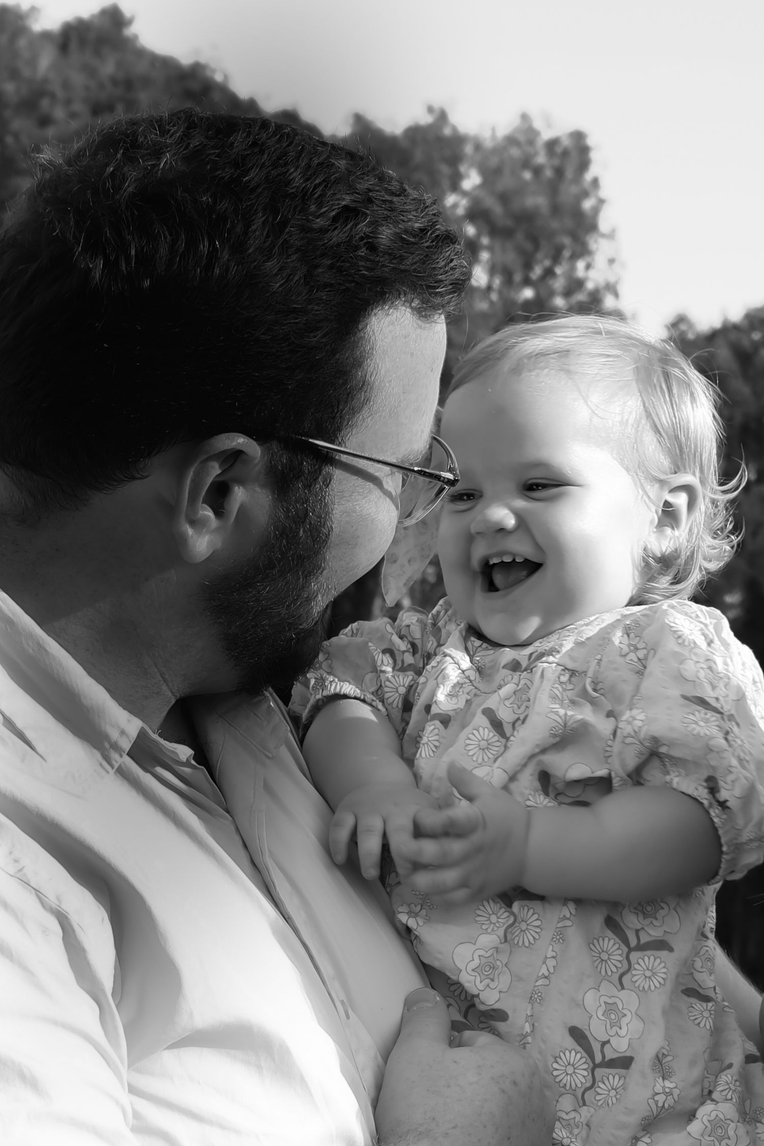 Black and white photo of a bearded father holding his laughing baby girl outdoors.