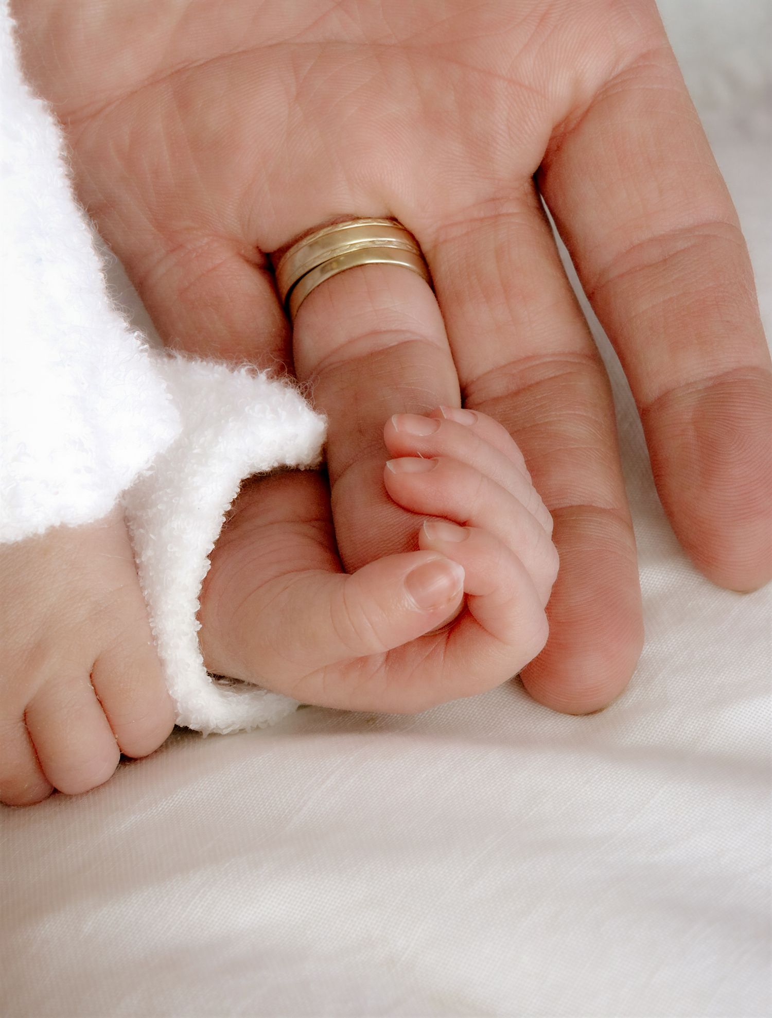 Infant's tiny hand reaches out to hold adult fingers with wedding band.