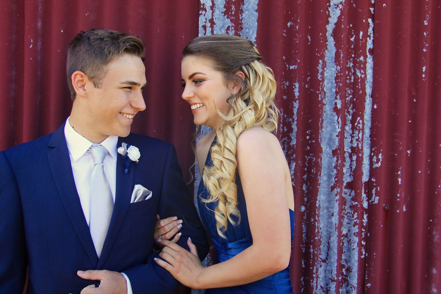 A couple in wedding attire poses intimately against a rustic red metal wall background.
