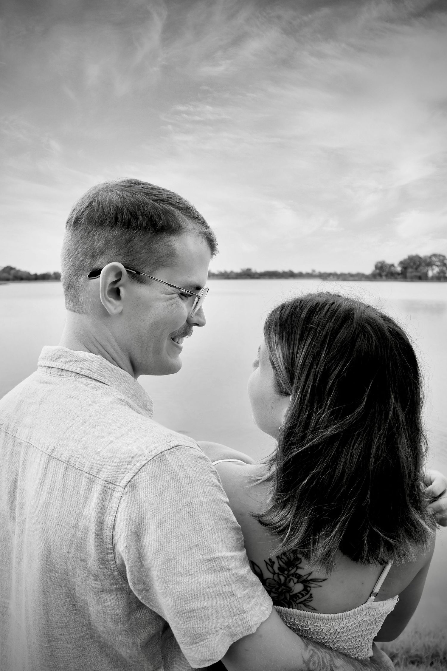 Couple in casual attire sharing an intimate moment by the water at sunset.