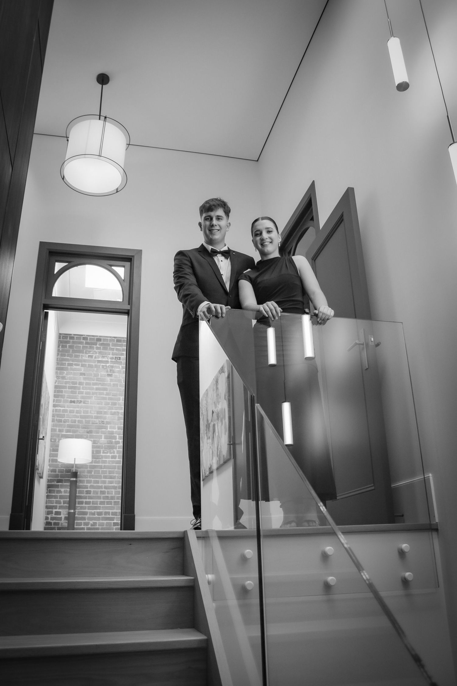 A creative black and white photo showing two people playfully posing on a staircase with angular walls.