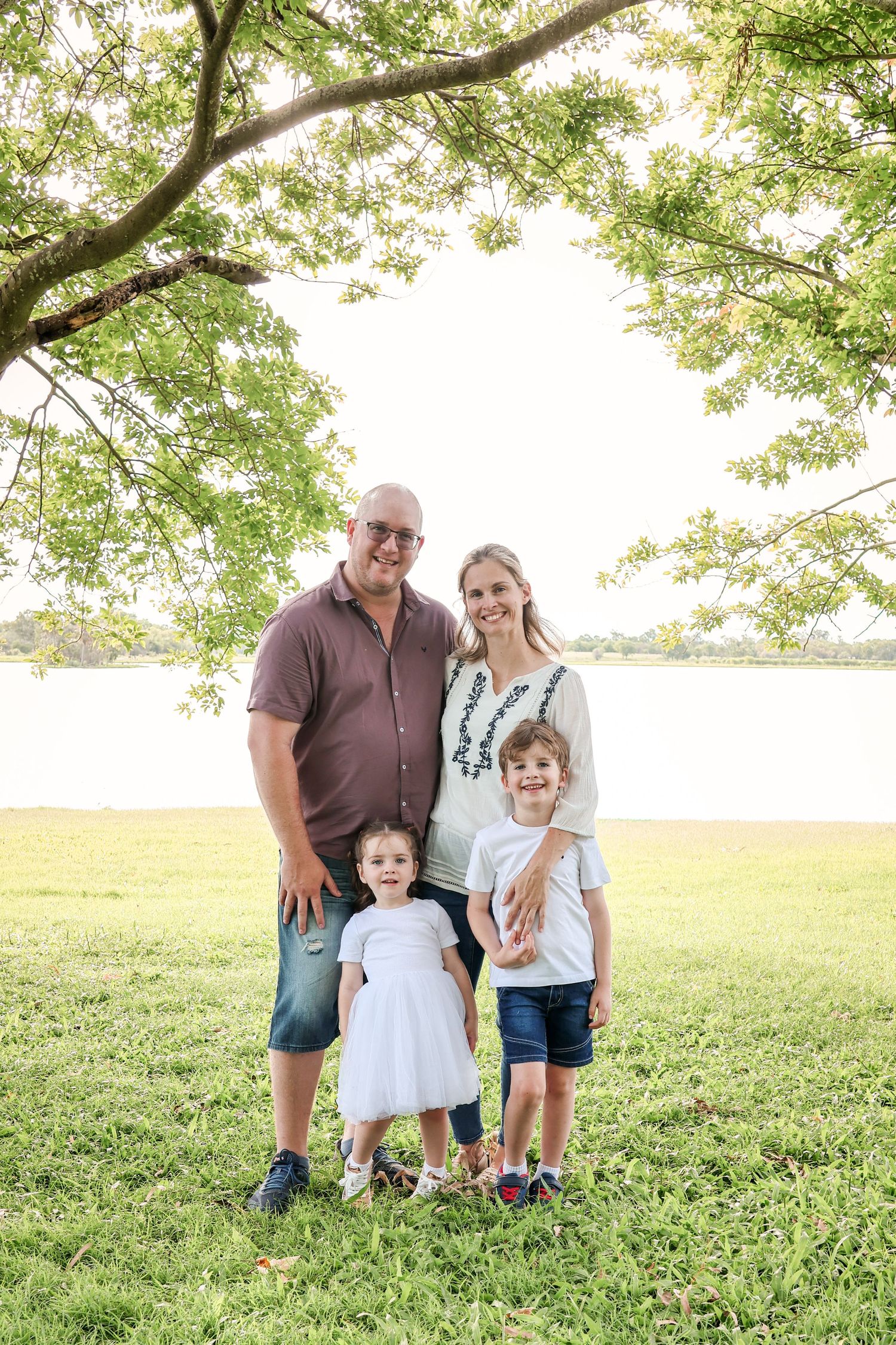 A family poses together on a grassy hill during a sunny summer day in a park.