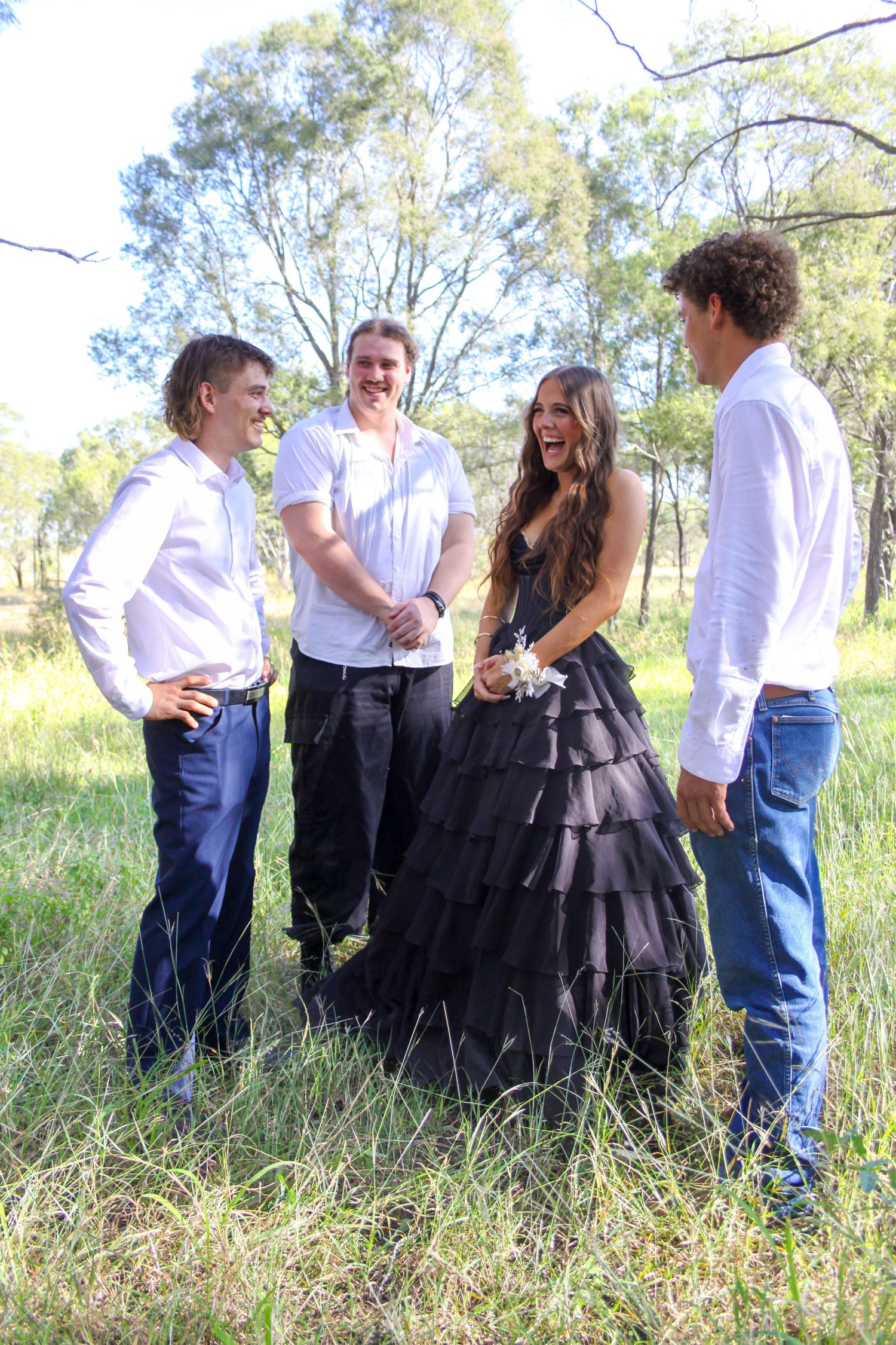 A group in white shirts and dark clothing poses together in a grassy field on a sunny day.