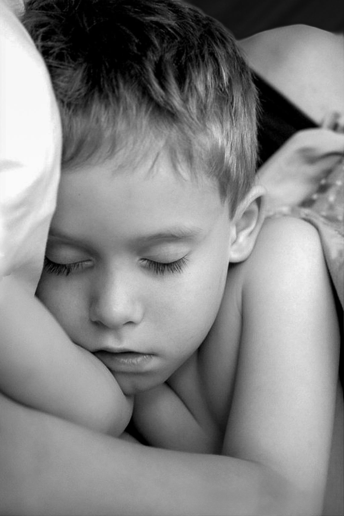 Black and white photo of a young boy resting peacefully with eyes closed, cradled in an adults arms.