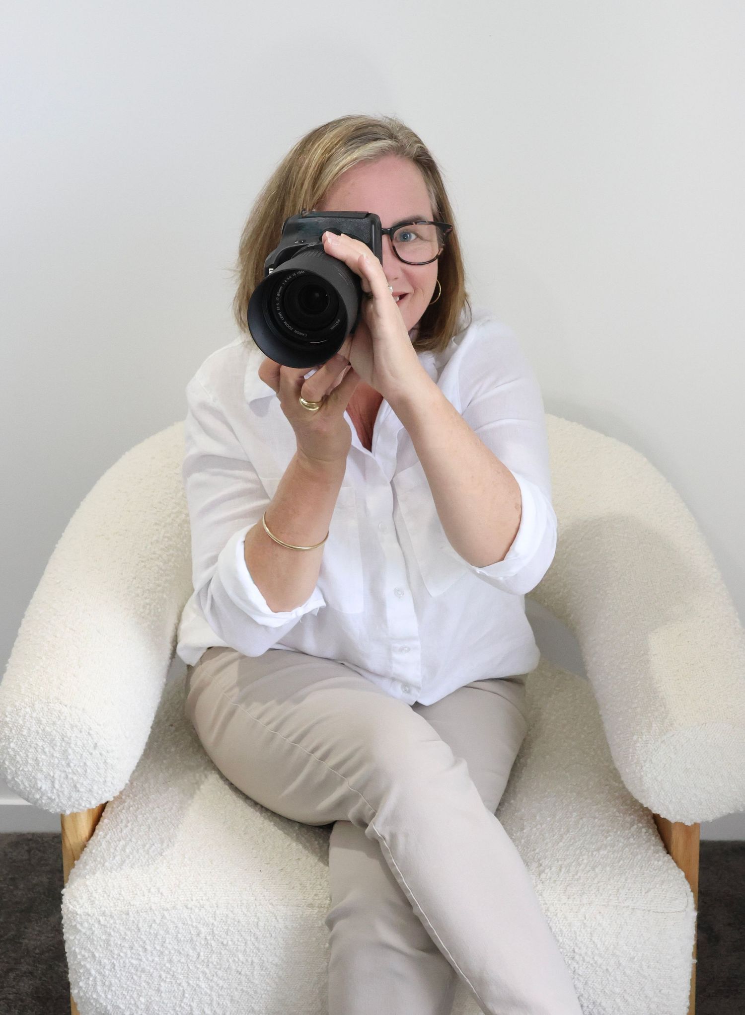 A person wearing glasses and a white shirt sits on a white couch in various relaxed poses with a camera.