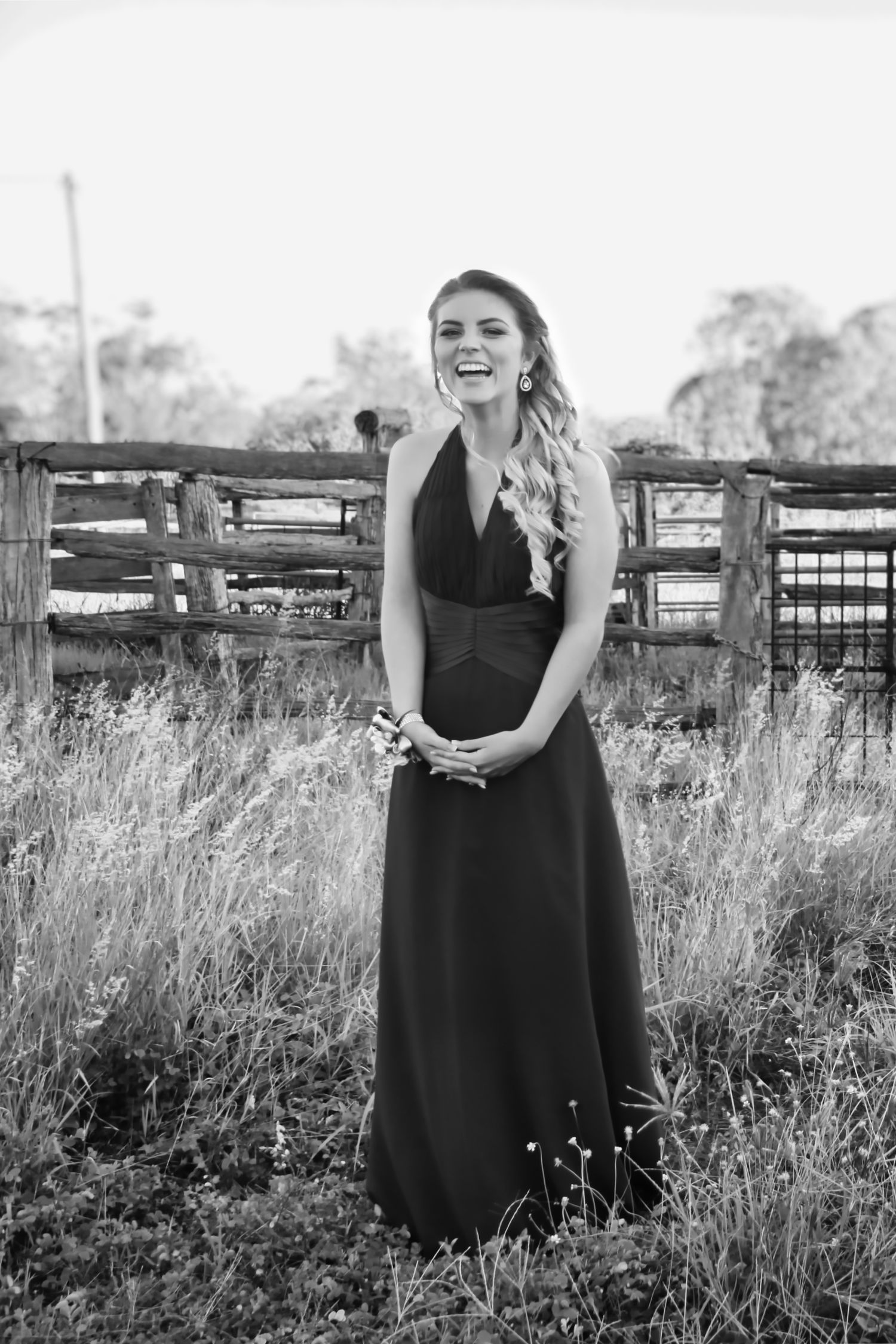 Black and white photo series showing someone in a black dress standing in a grassy field with wooden fences.