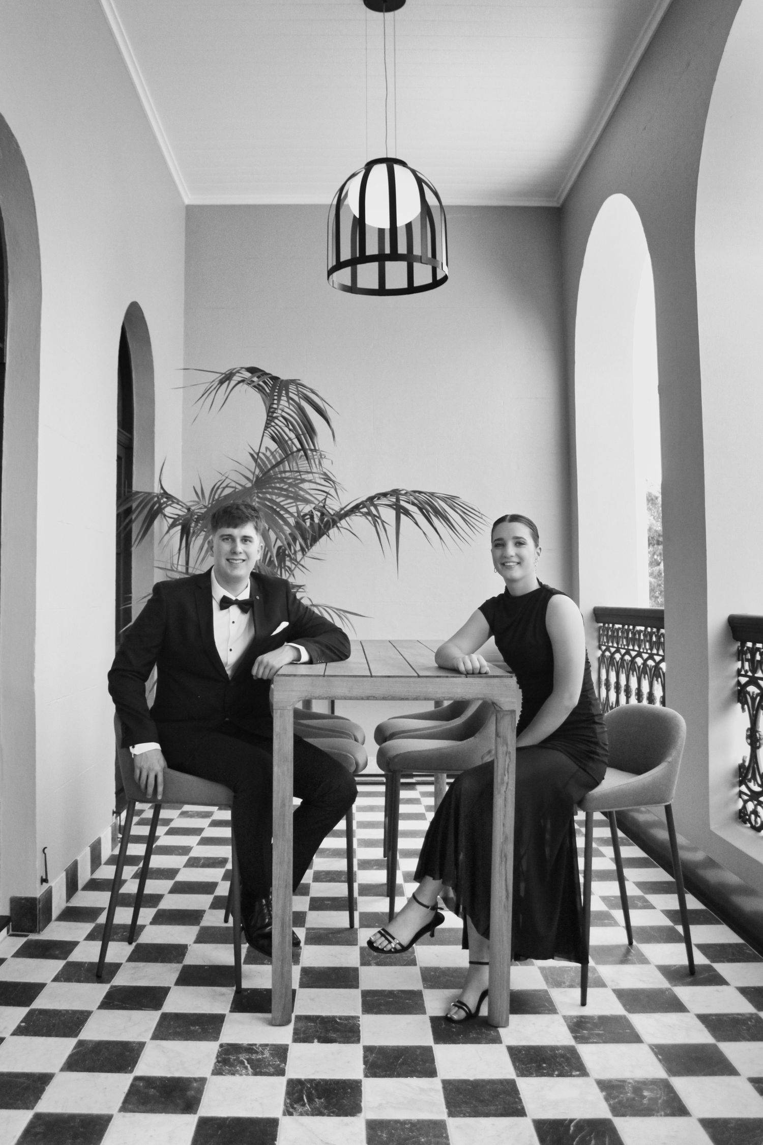 Black and white surreal photo of people posing in creative positions on a checkered floor with white columns.