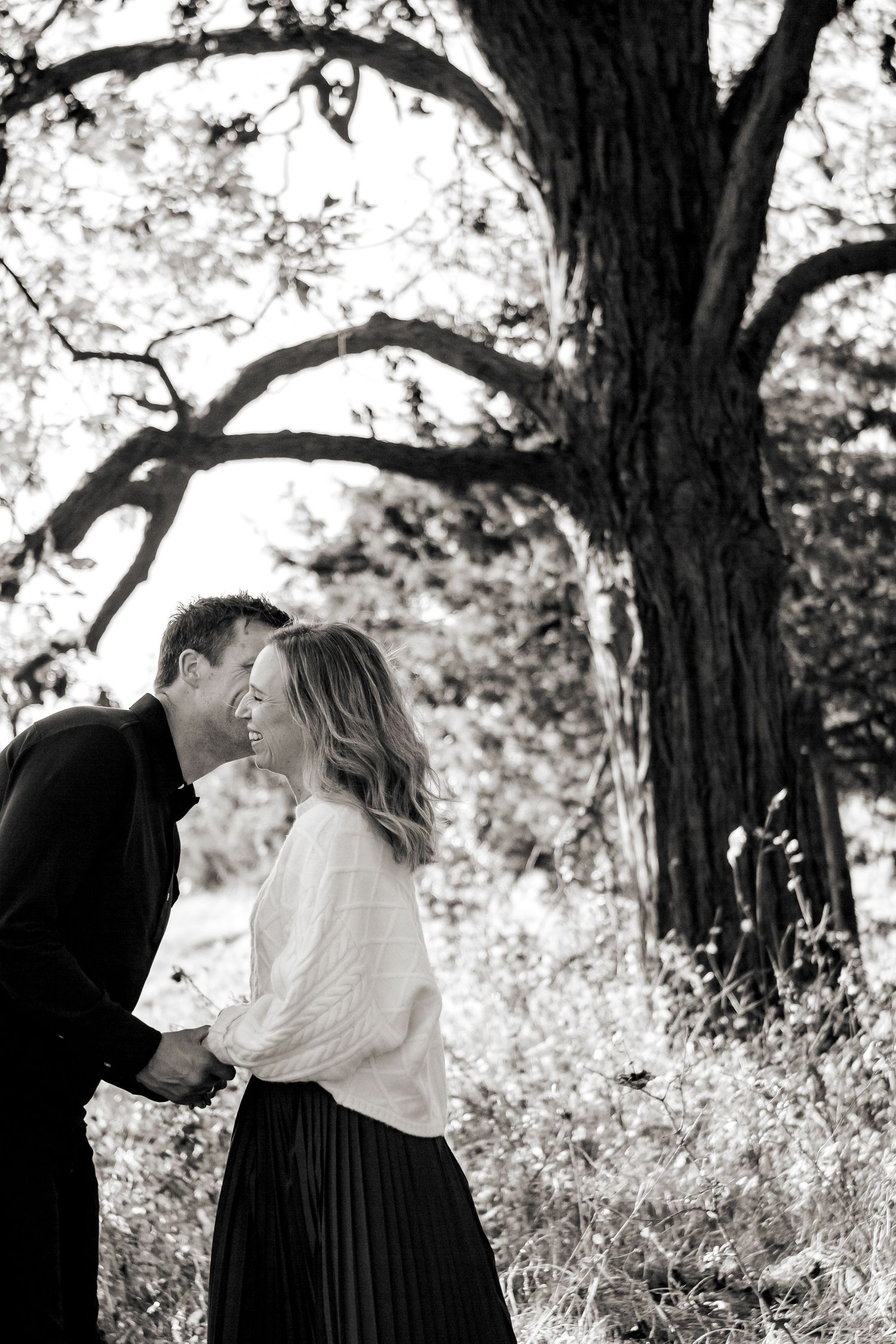 A romantic black and white photo series showing a couple embracing under trees in a natural outdoor setting at a Lake Country Family session