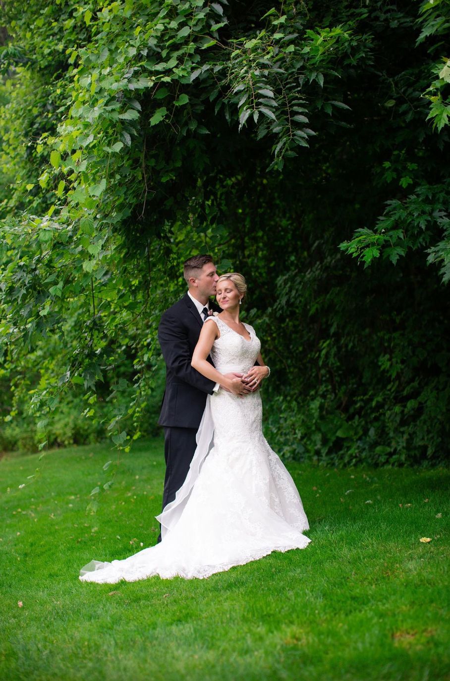 Wedding couple poses on lush green lawn for romantic portraits.