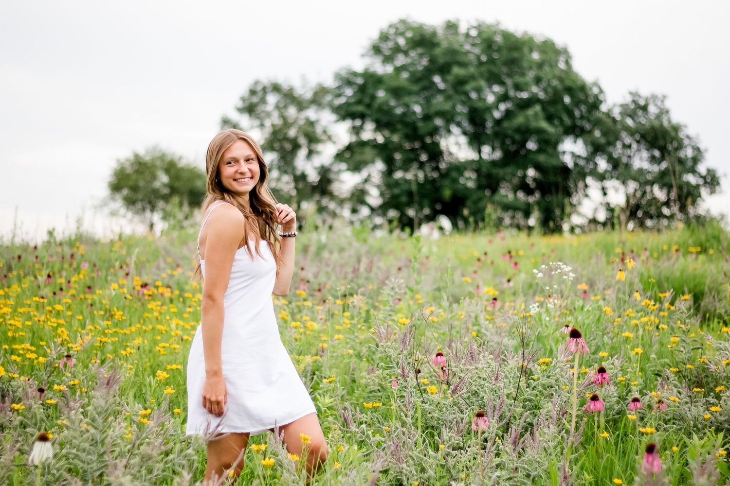 Woman in white sundress walks through wildflower meadow on sunny summer day.