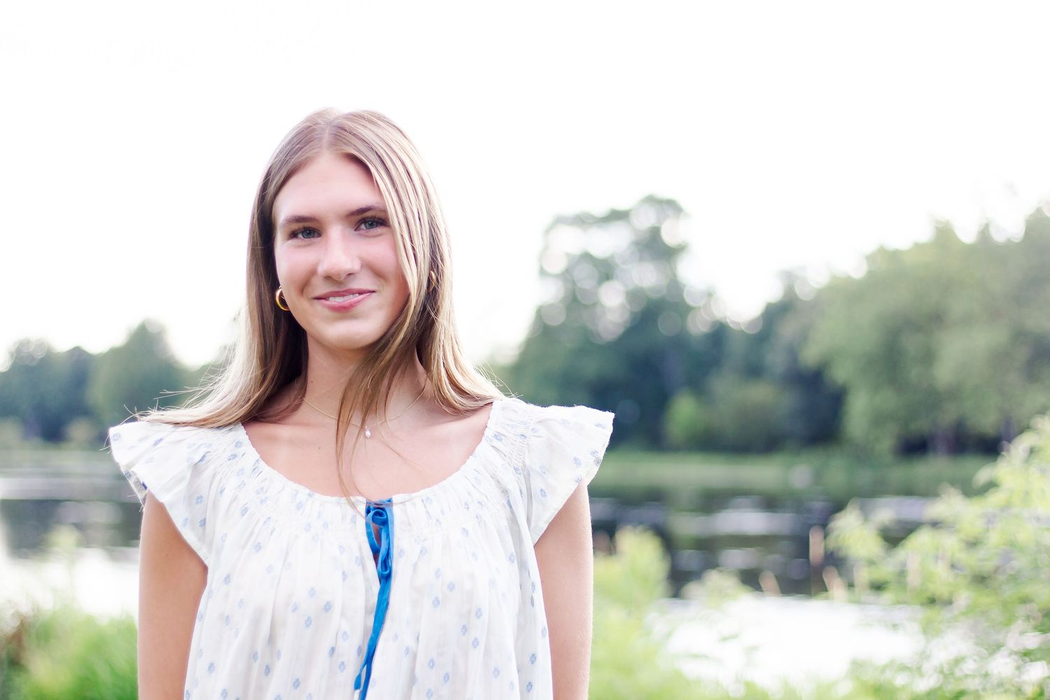 A bright summer portrait by the water wearing a white dress with flutter sleeves.