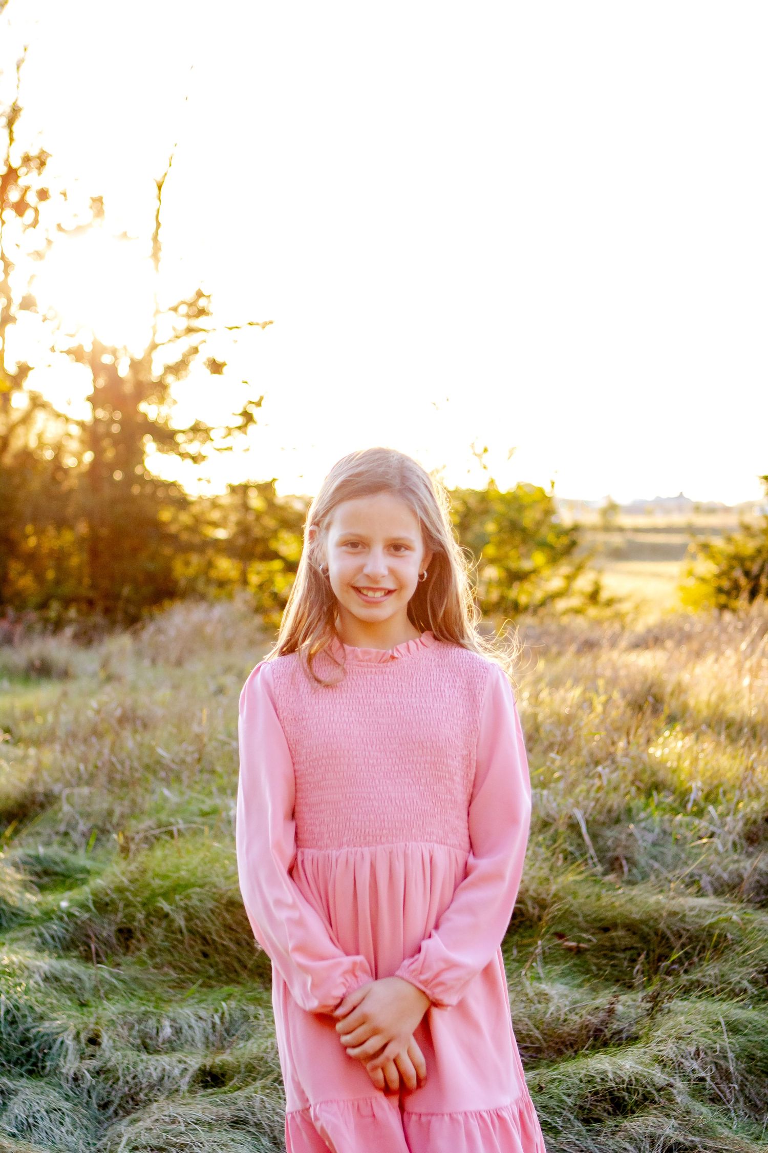 A pink-dressed figure stands in a sunlit meadow during golden hour with warm backlighting and natural scenery