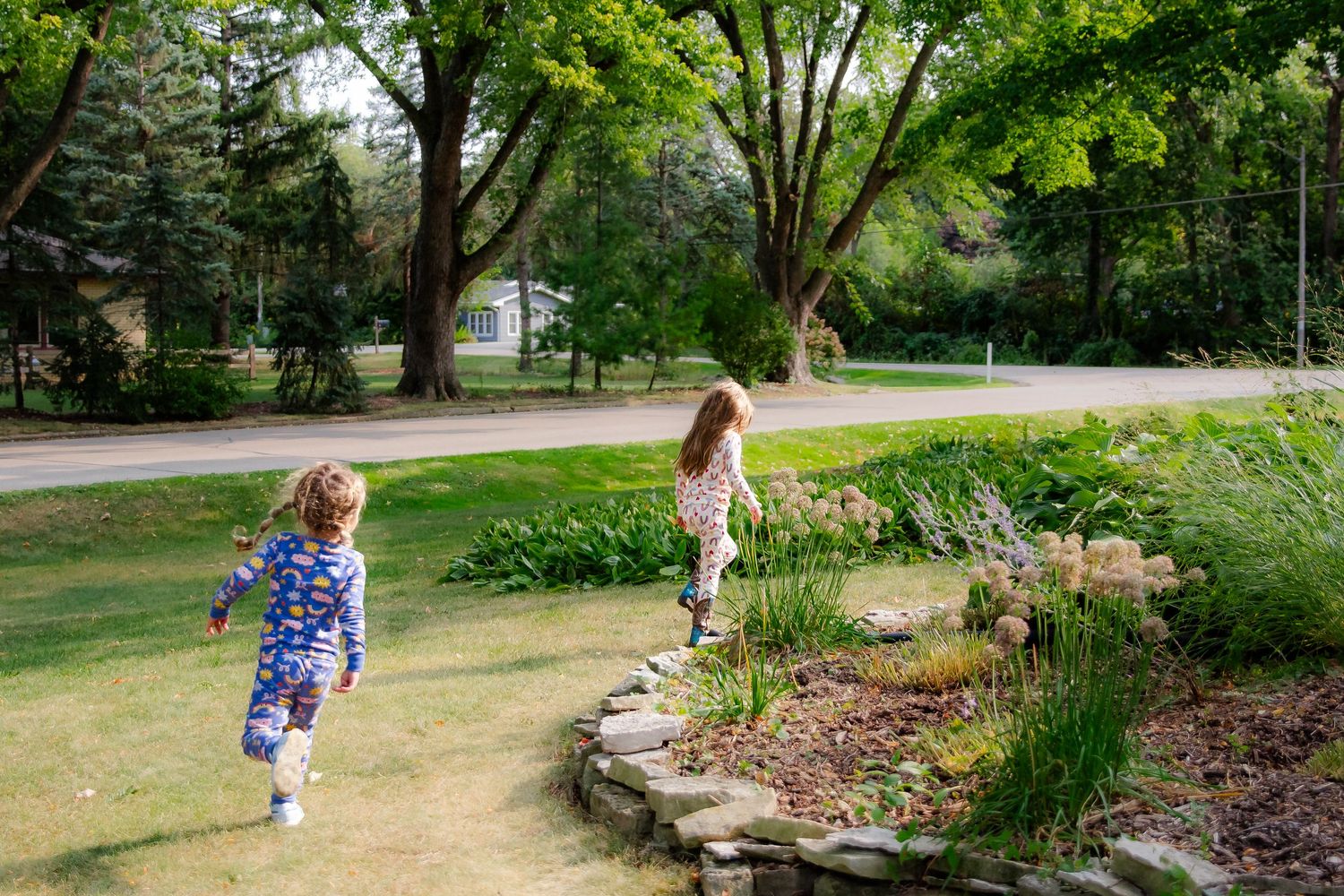 Two children explore a winding garden path bordered by lush greenery and stone landscaping on a sunny day at Delafield home session