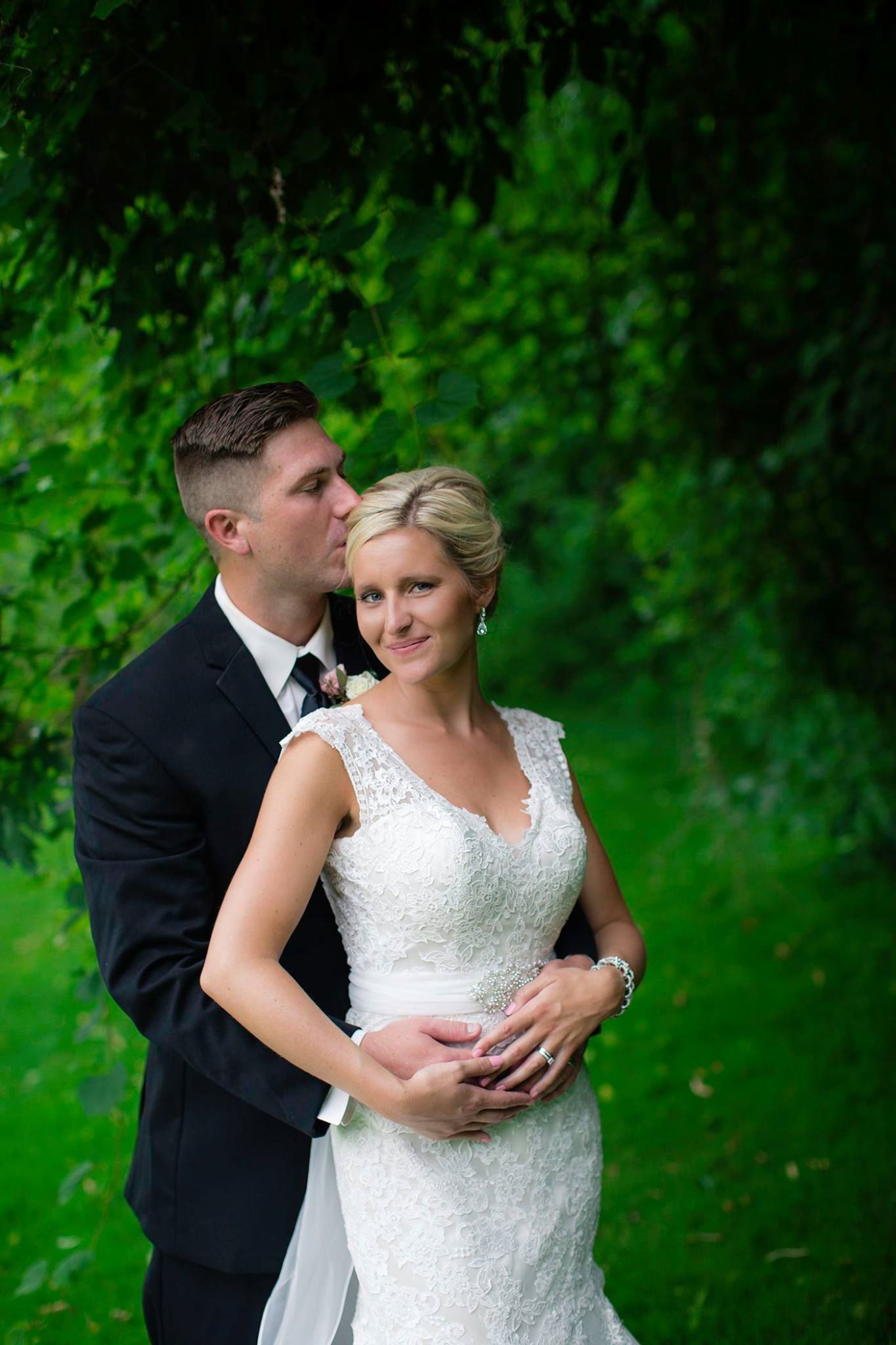 A romantic wedding portrait of a couple embracing outdoors with lush green foliage in the background.