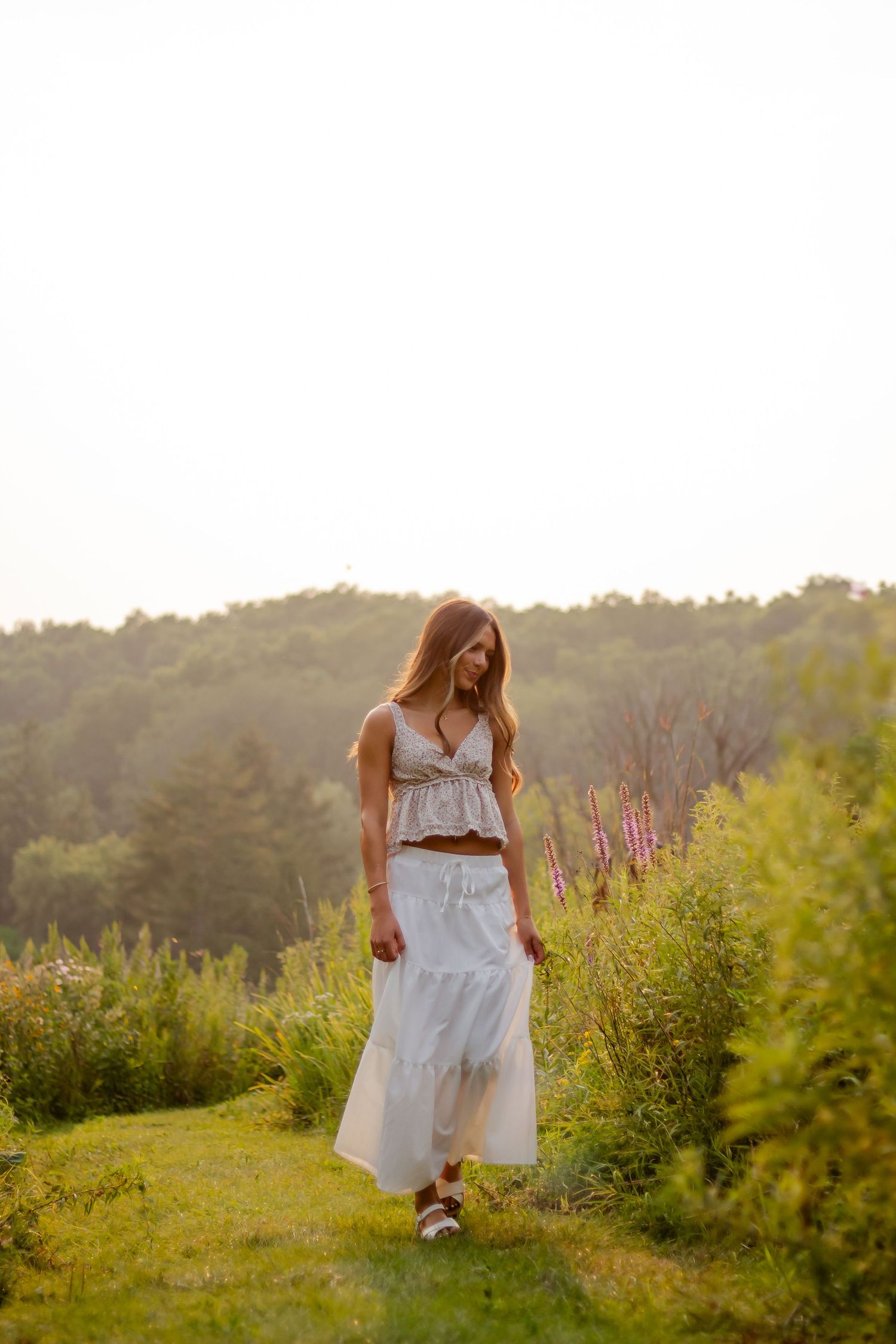 A white flowy dress contrasts beautifully against a lush green meadow at golden hour.