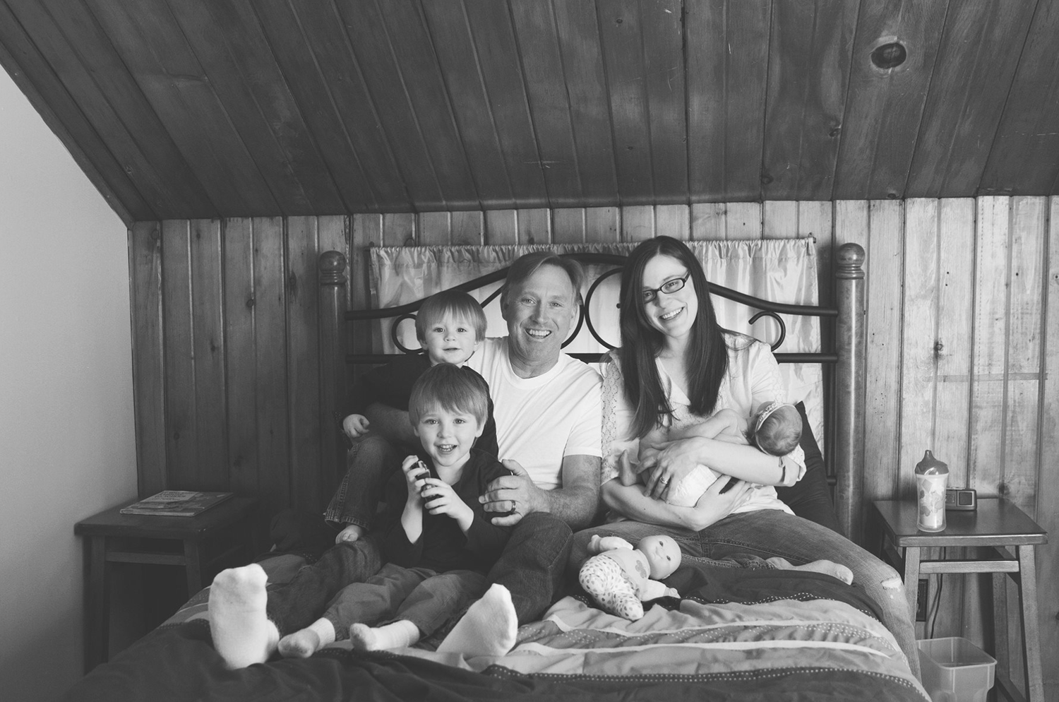 A family relaxing together on a bed in a rustic wood-paneled room.