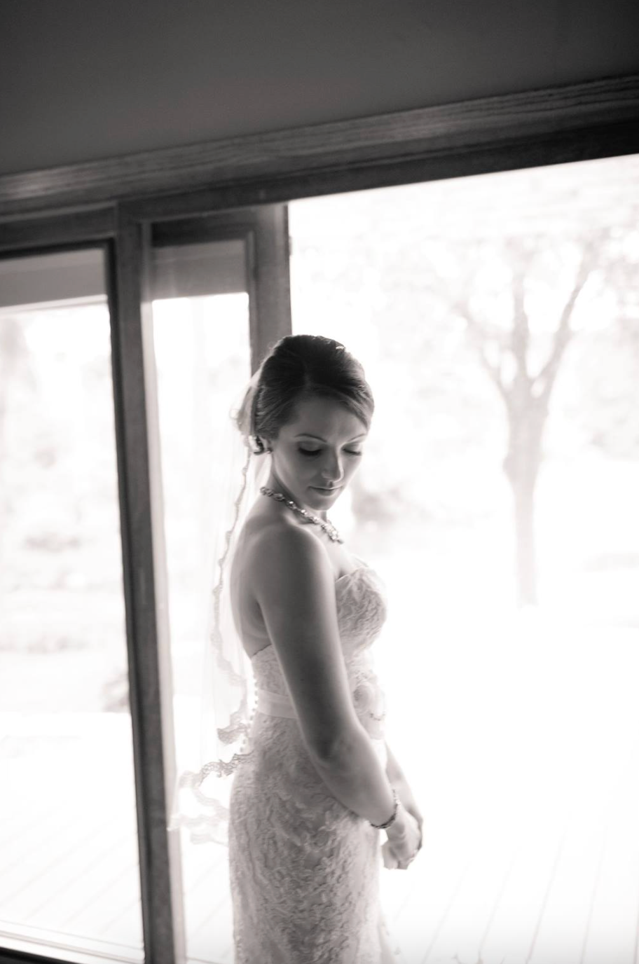 A silhouetted figure in a lace wedding dress stands by a window in dramatic black and white lighting.