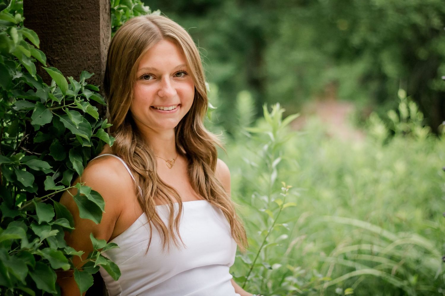 Summer portrait of woman in white tank top against lush green garden background.