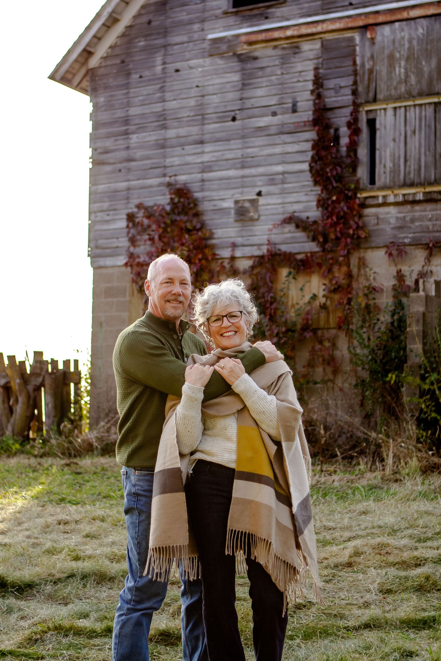 Husband and wife pose outside of barn during fall photo session in Oconomowoc