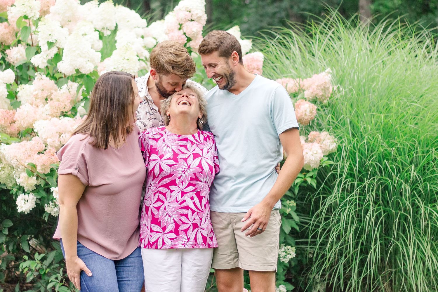 A group stands together sharing a warm moment in front of pink hydrangea bushes and ornamental grasses at Delafield home session