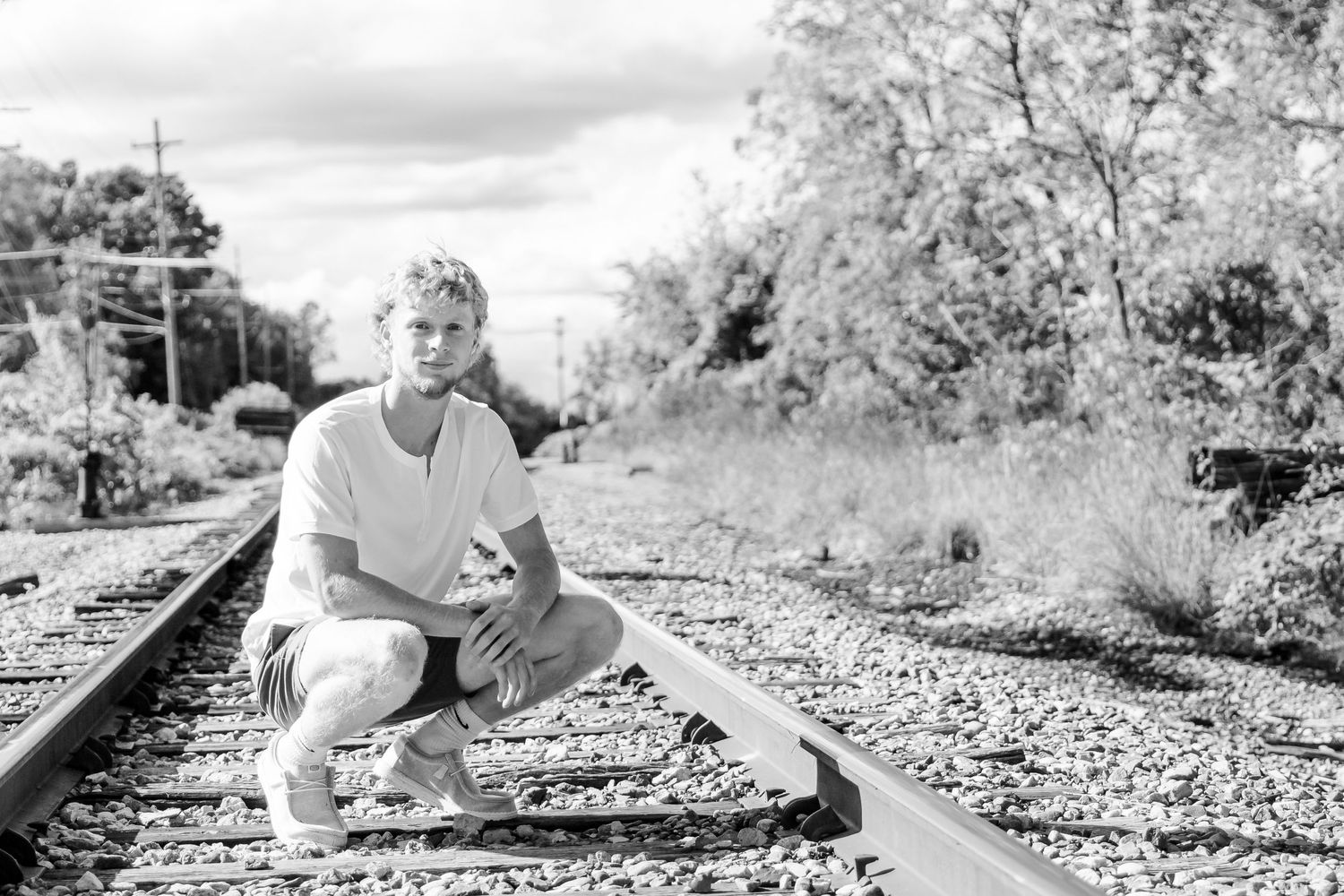 Black and white photos showing a couple sitting and posing playfully along railroad tracks in nature during a Michigan senior session
