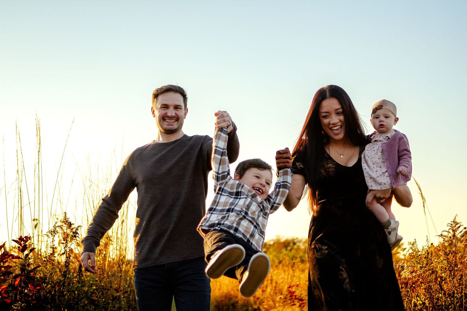Family playing and laughing together in a golden sunlit field at dusk.