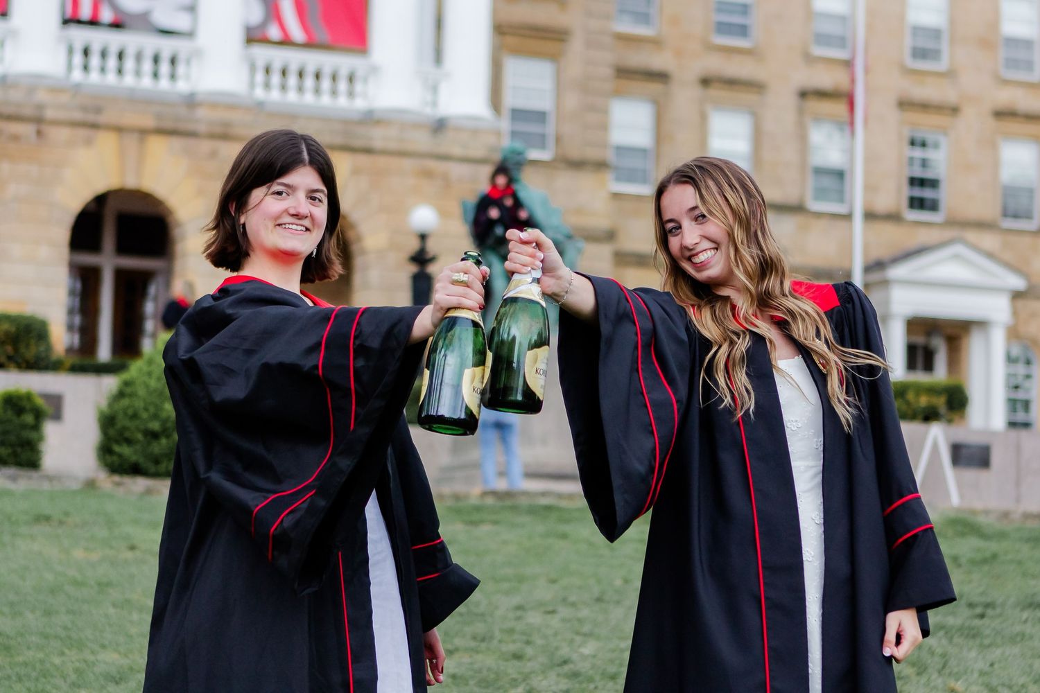 Graduates in black robes and caps celebrate together on university campus.