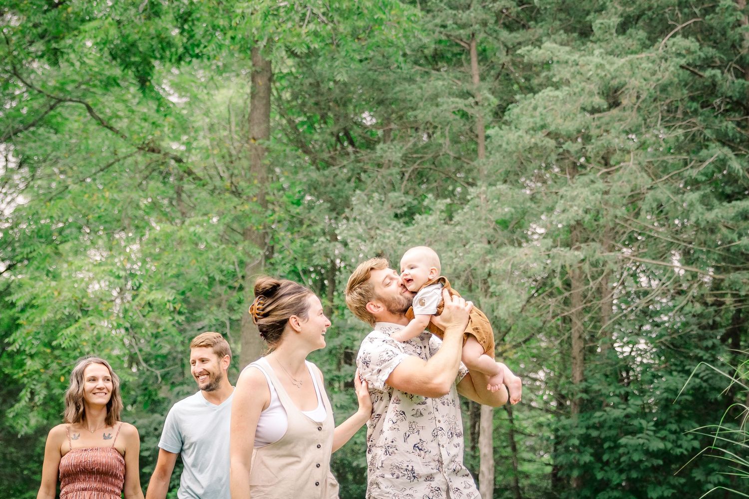 Wedding party poses together in a lush garden setting with green trees and flowers in the background at Delafield home session