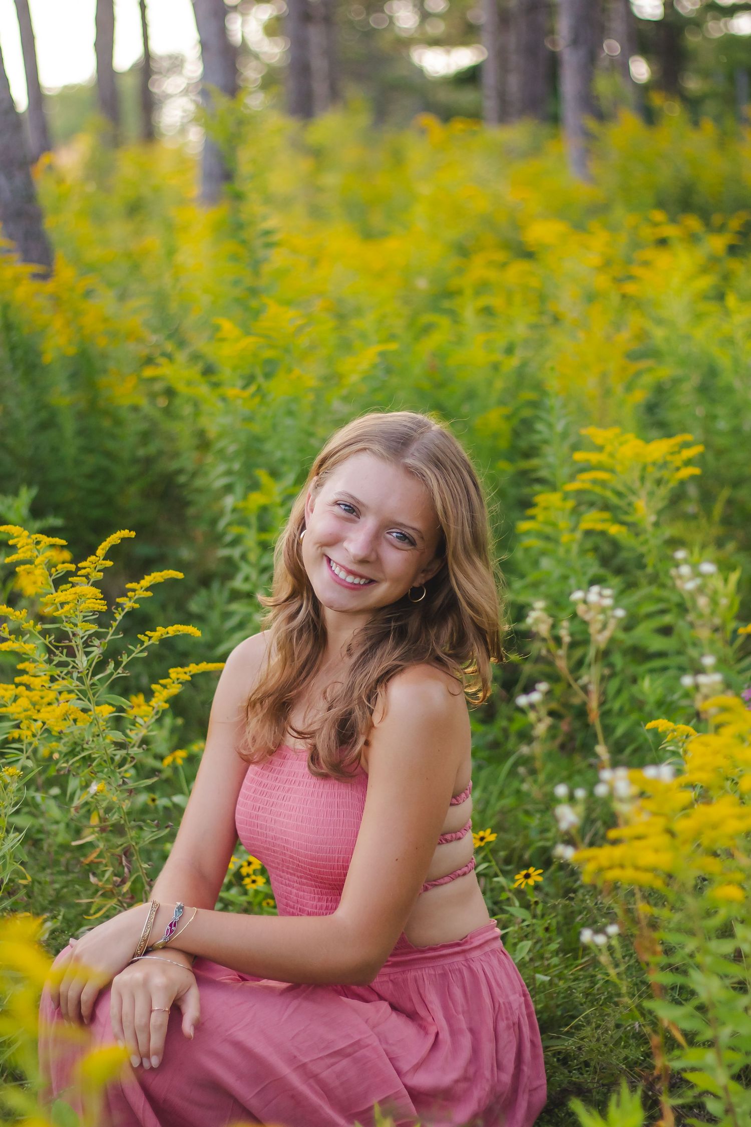Pink-dressed figure posing gracefully among vibrant yellow wildflowers in a sunlit forest.