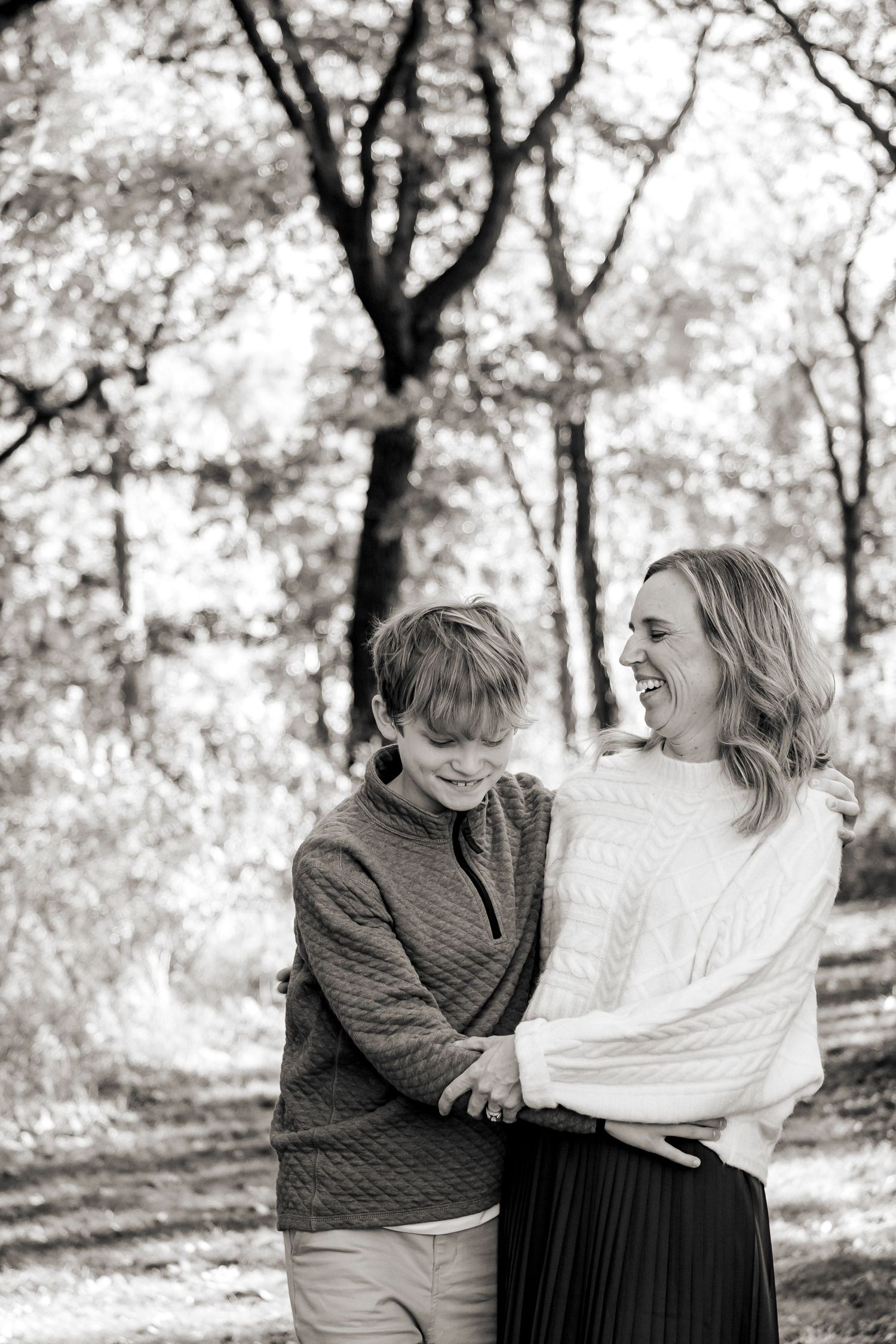 Two people share joyful laughter while sitting together outdoors in a black and white nature setting at an Oconomowoc family session