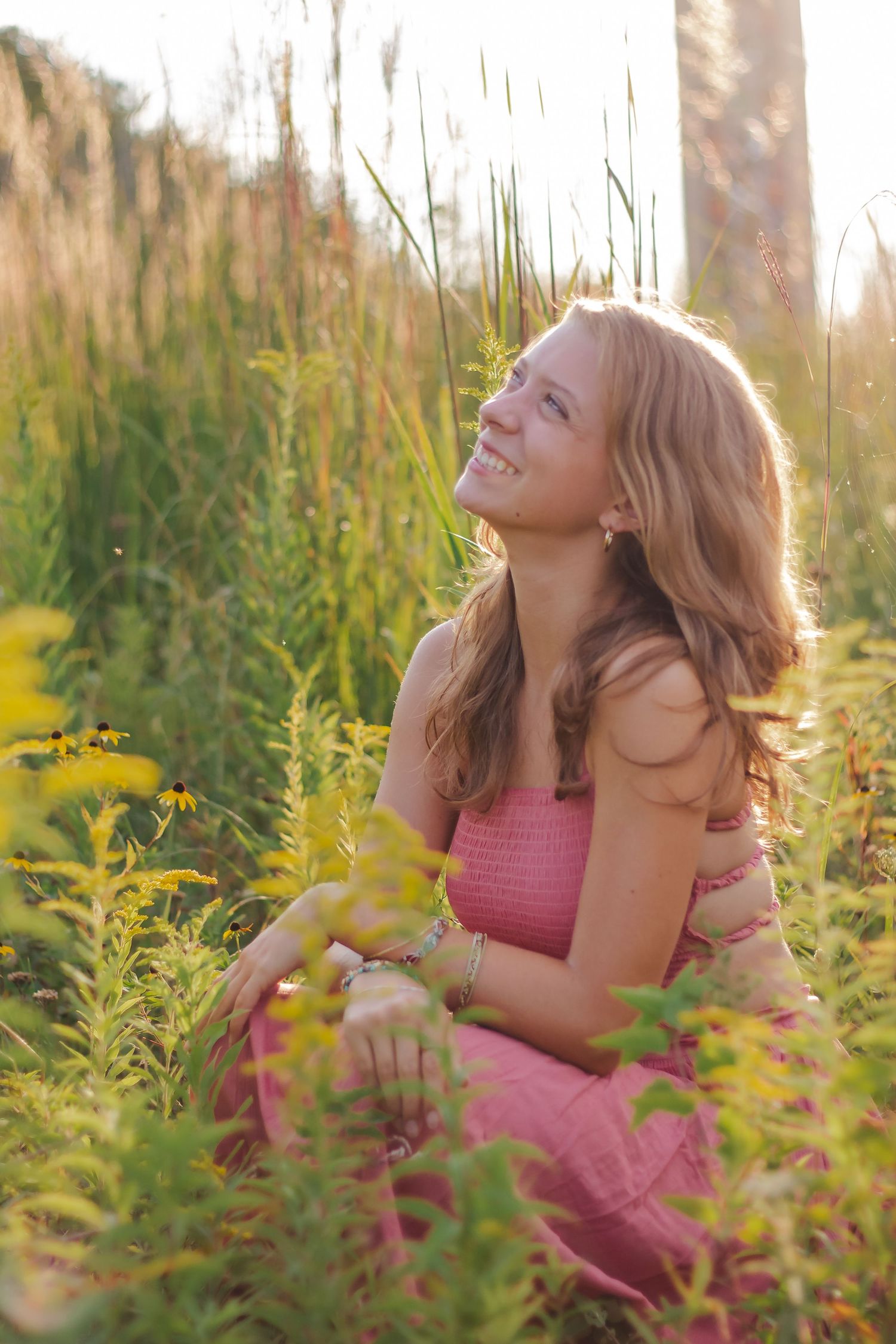 Figure in pink dress lying among tall yellow wildflowers during golden hour.