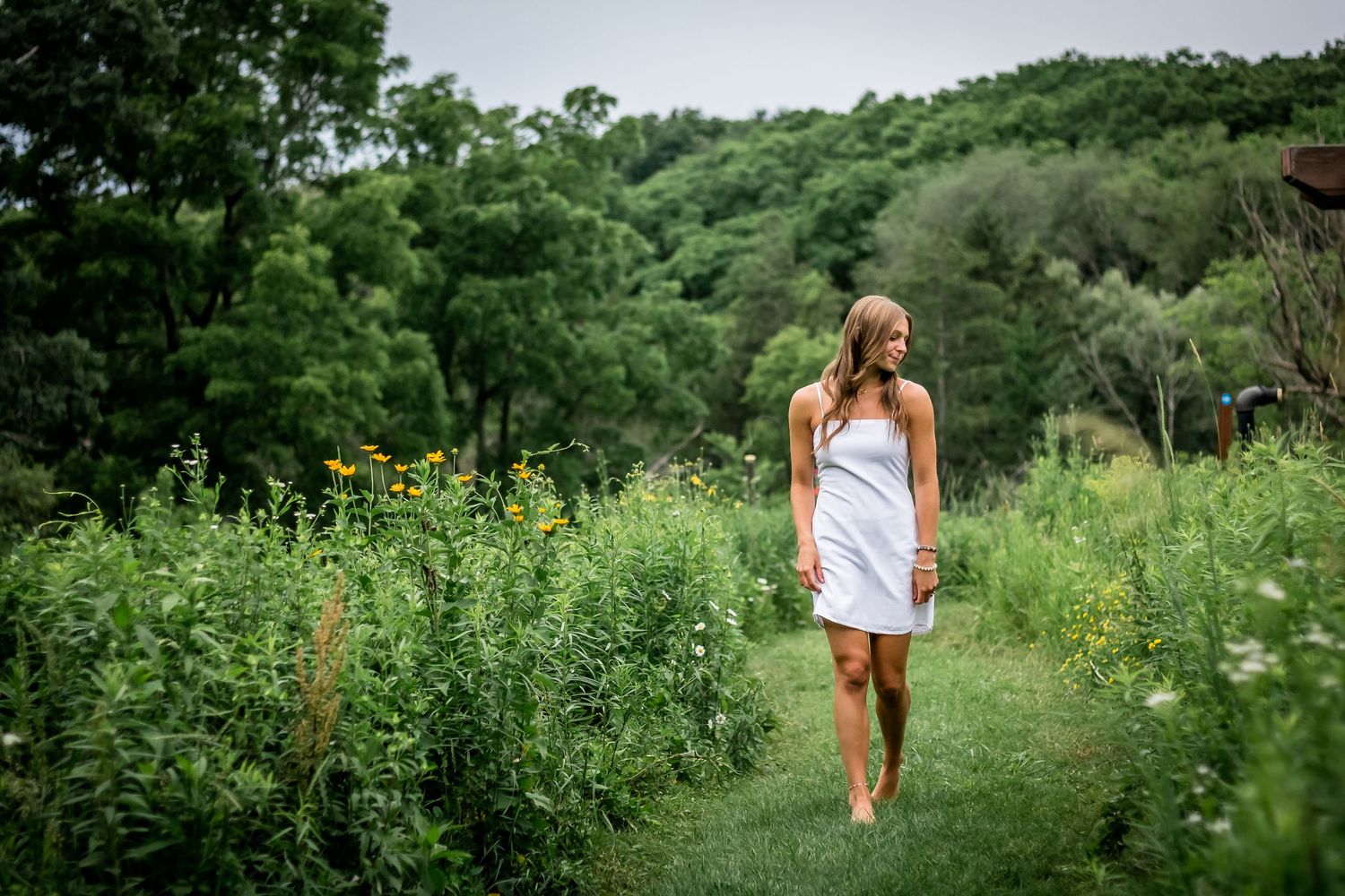 Woman in white dress walks along nature trail surrounded by lush green vegetation.