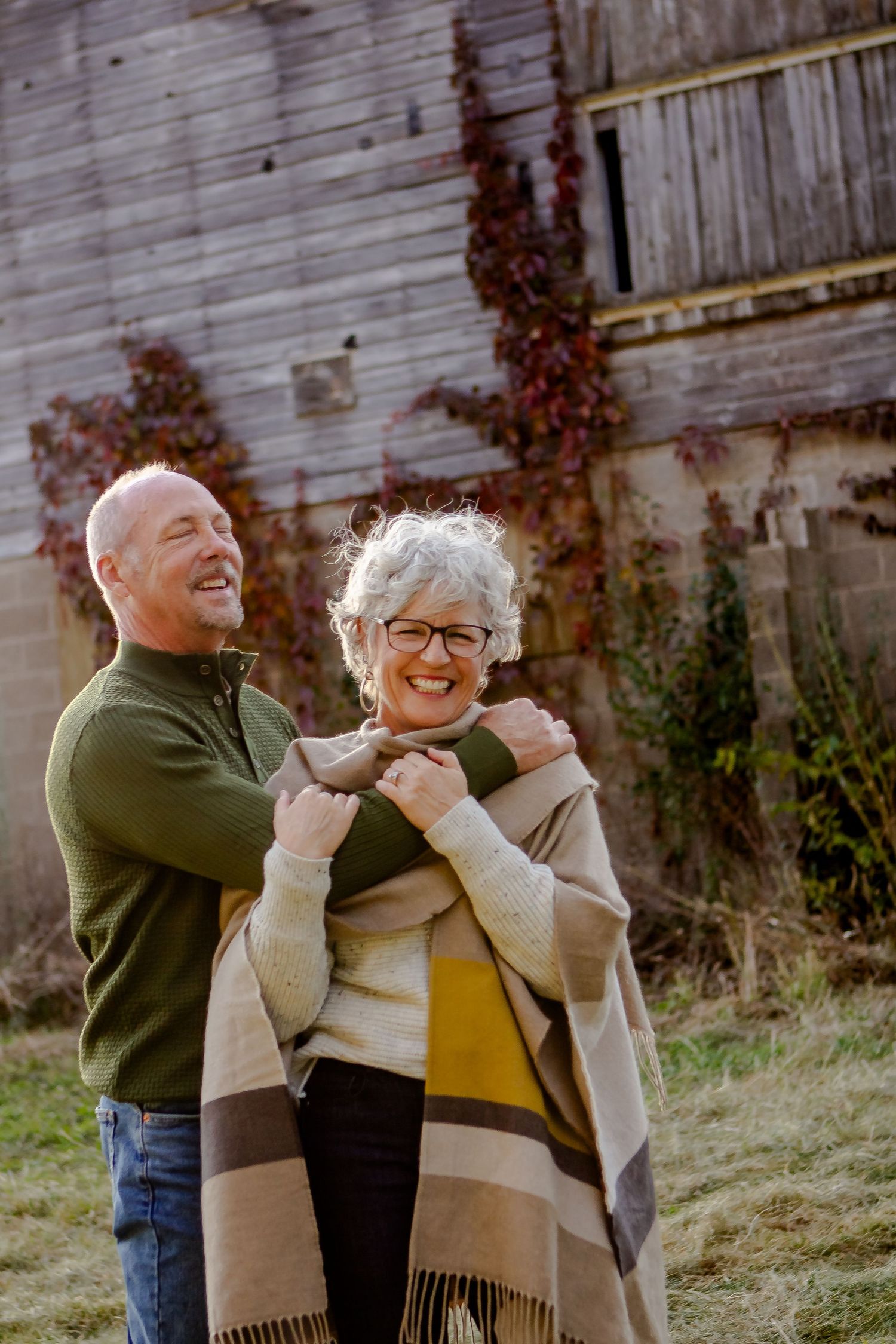 Husband and wife hug and laugh outside of barn during fall photo session in Oconomowoc