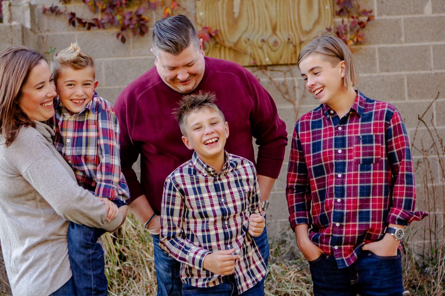 Family group wearing coordinated plaid shirts posing against rustic barn wall.