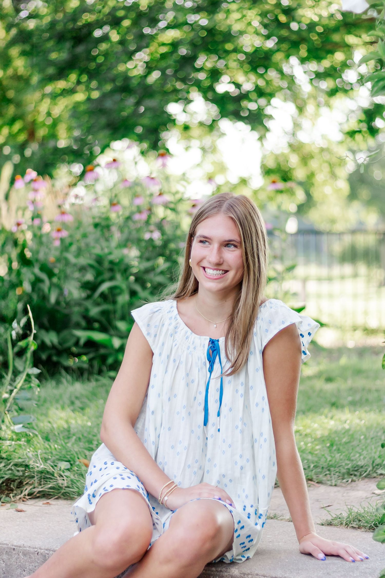 A casual outdoor portrait sitting on stone steps in a white summer dress.