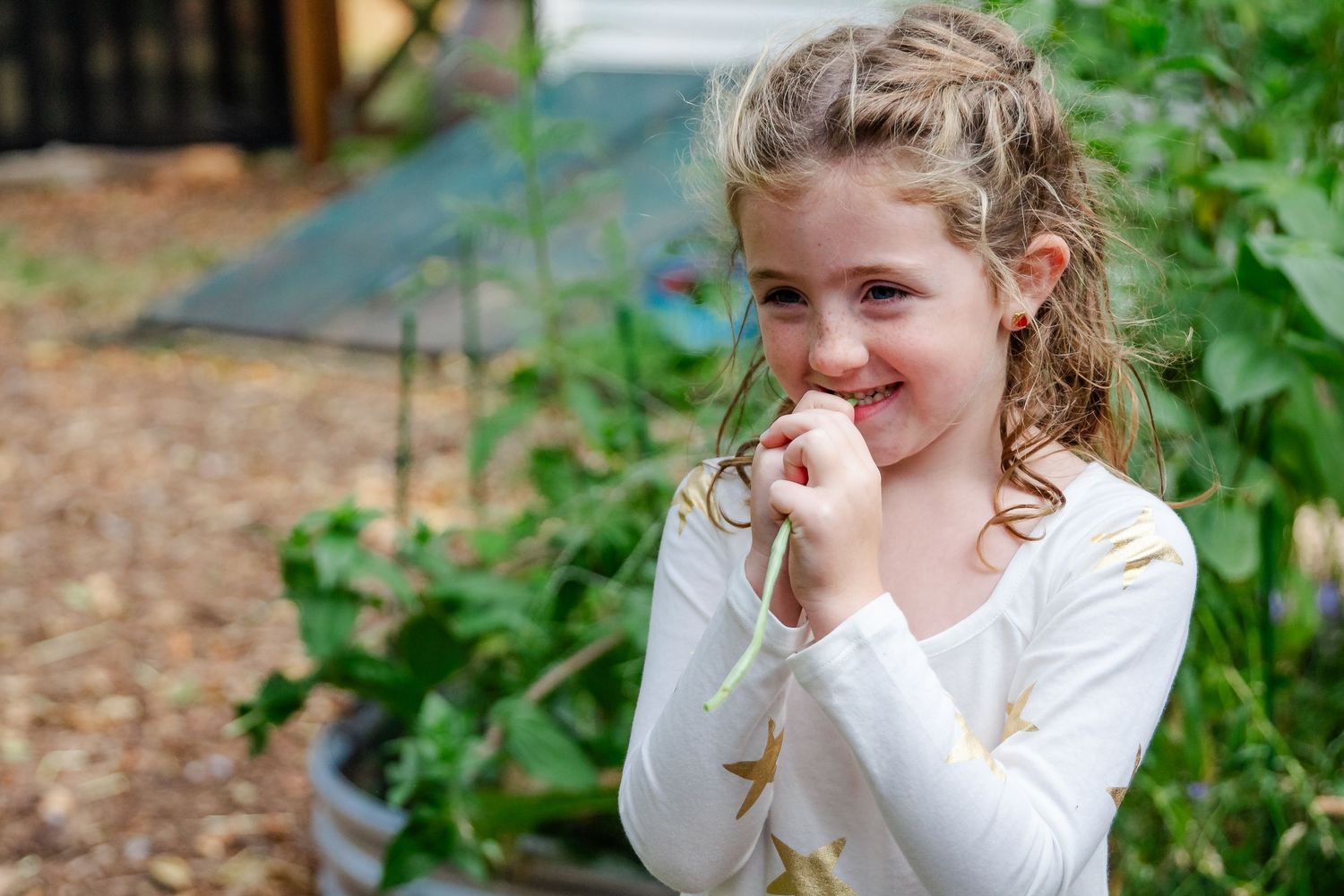 Young girl giggling in garden setting with curly hair.