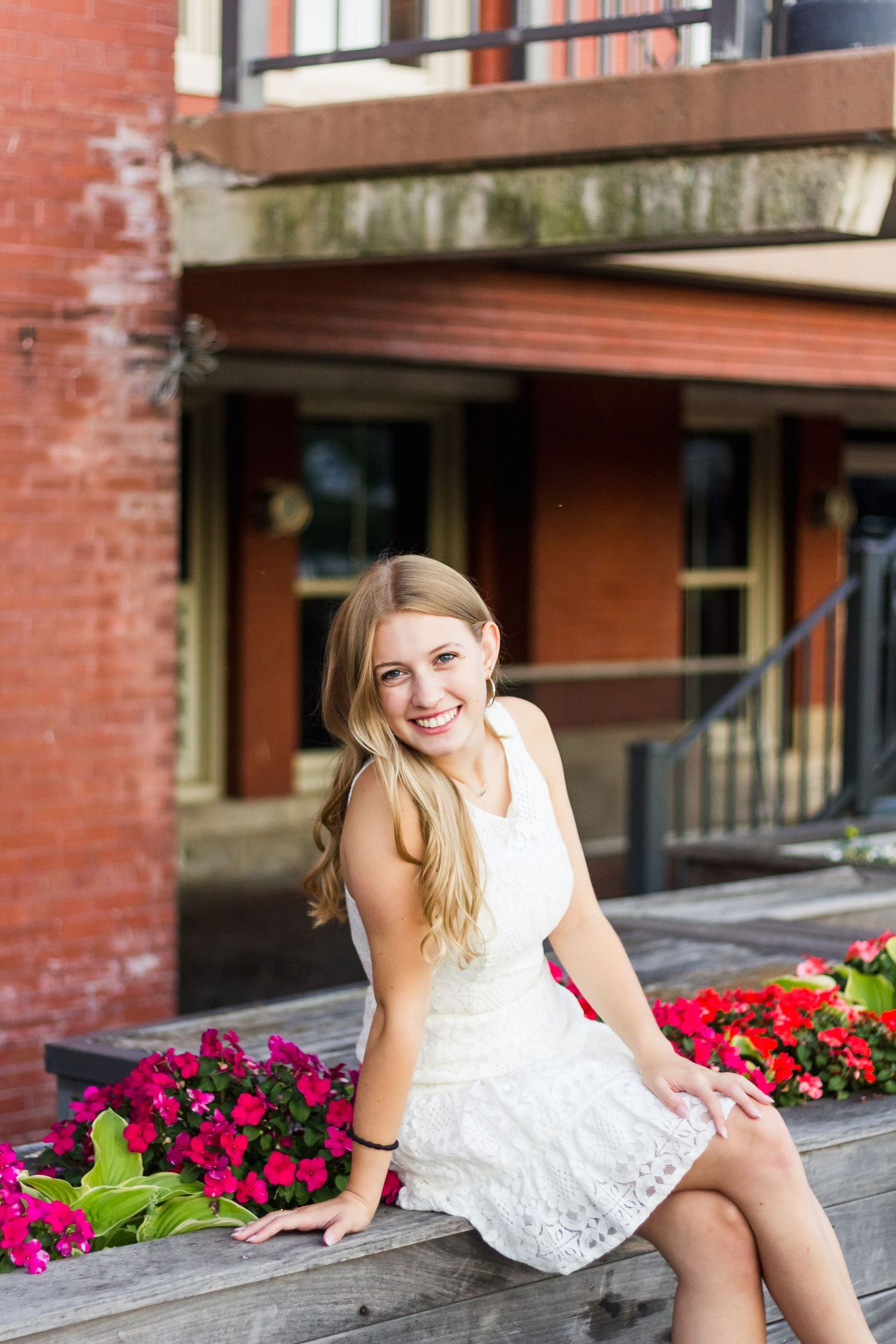 Portrait on steps with bright red flowers and brick building backdrop.