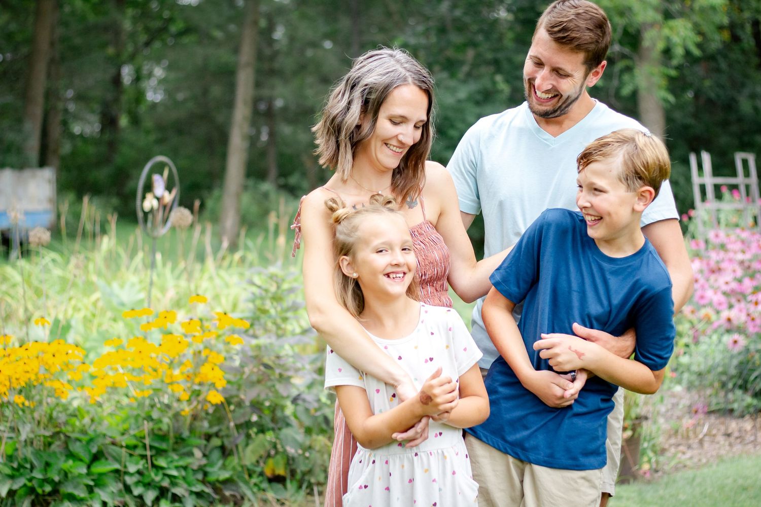 A family enjoys a playful moment together in a vibrant garden filled with colorful summer flowers at Delafield home session