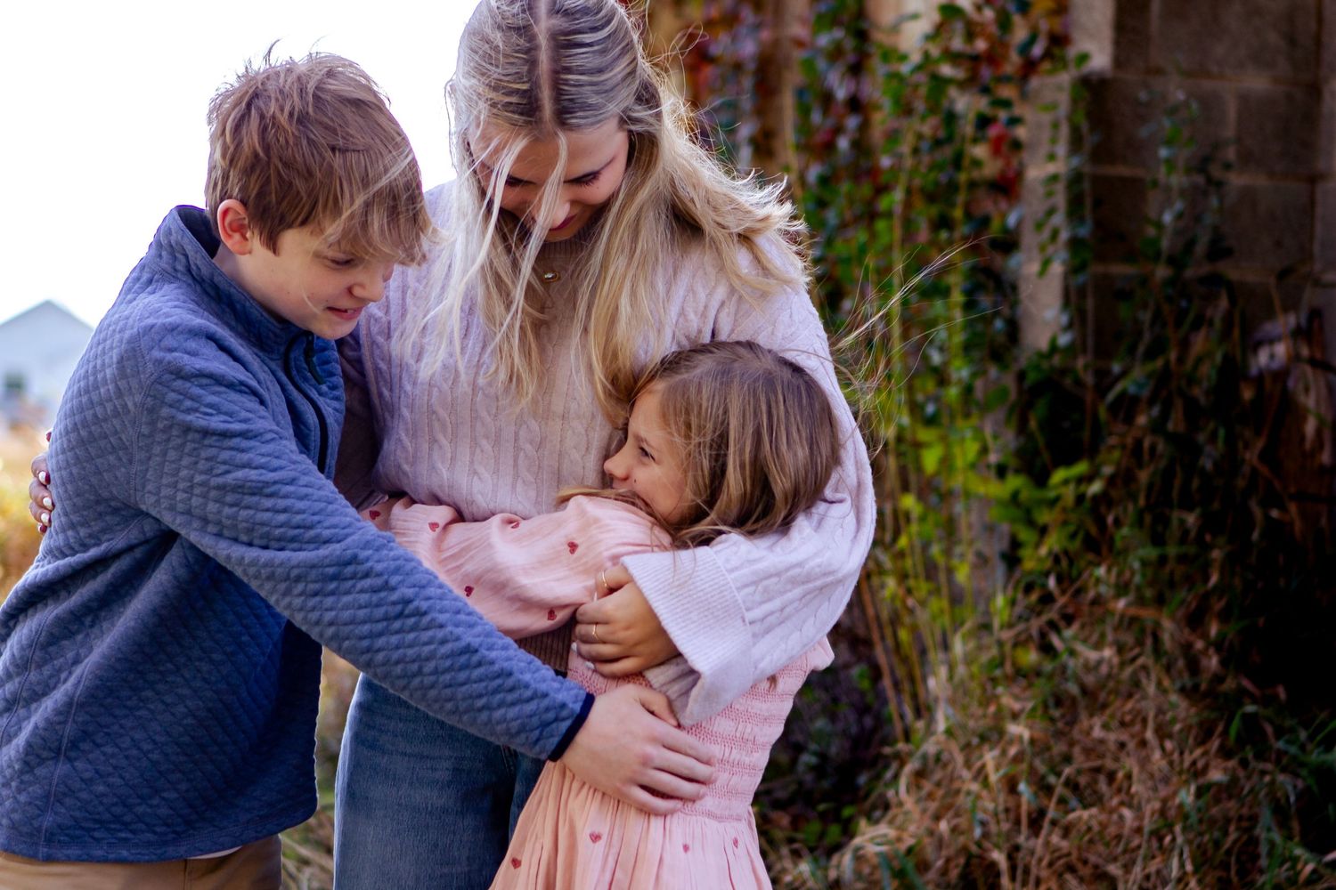 Family shares tender embraces in a series of outdoor autumn portraits against natural foliage at a Lake Country Family session