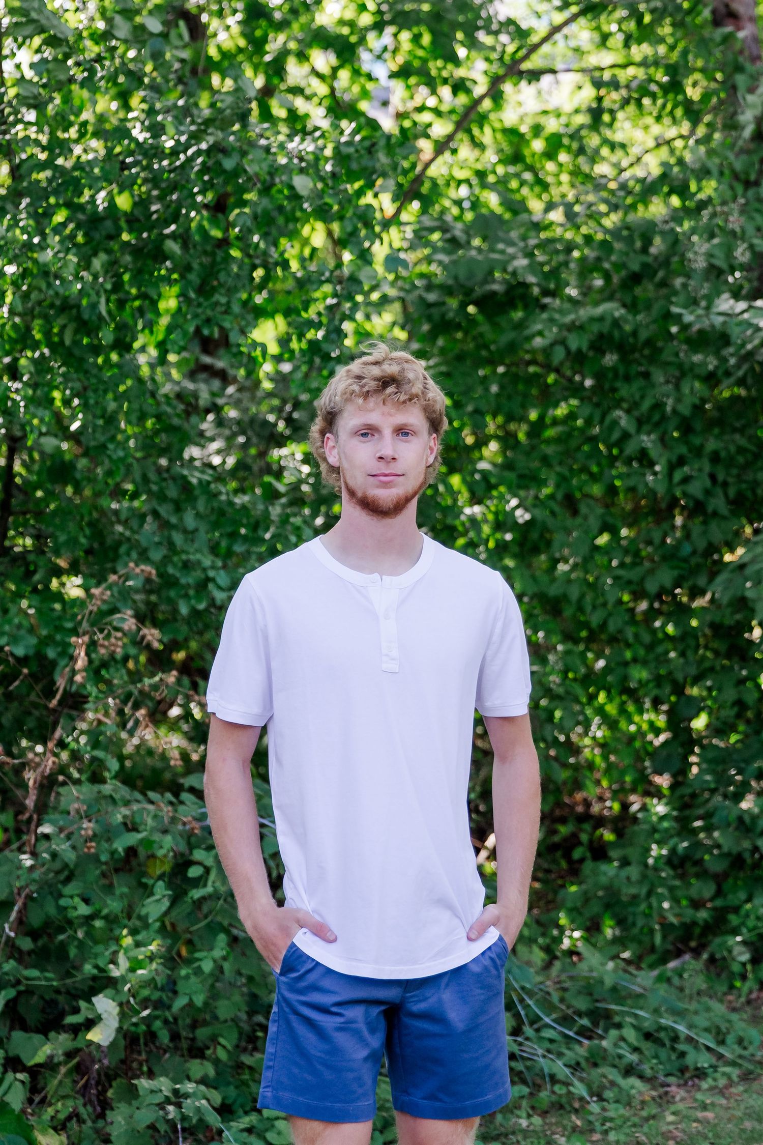 Summer portrait session with white t-shirt and blue shorts against green foliage.