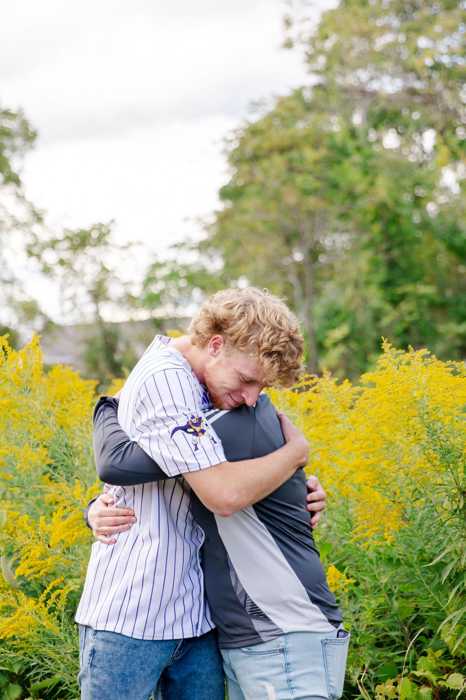 Mom and son embracing in a field of blooming yellow goldenrod flowers on a sunny autumn day during a Michigan senior session