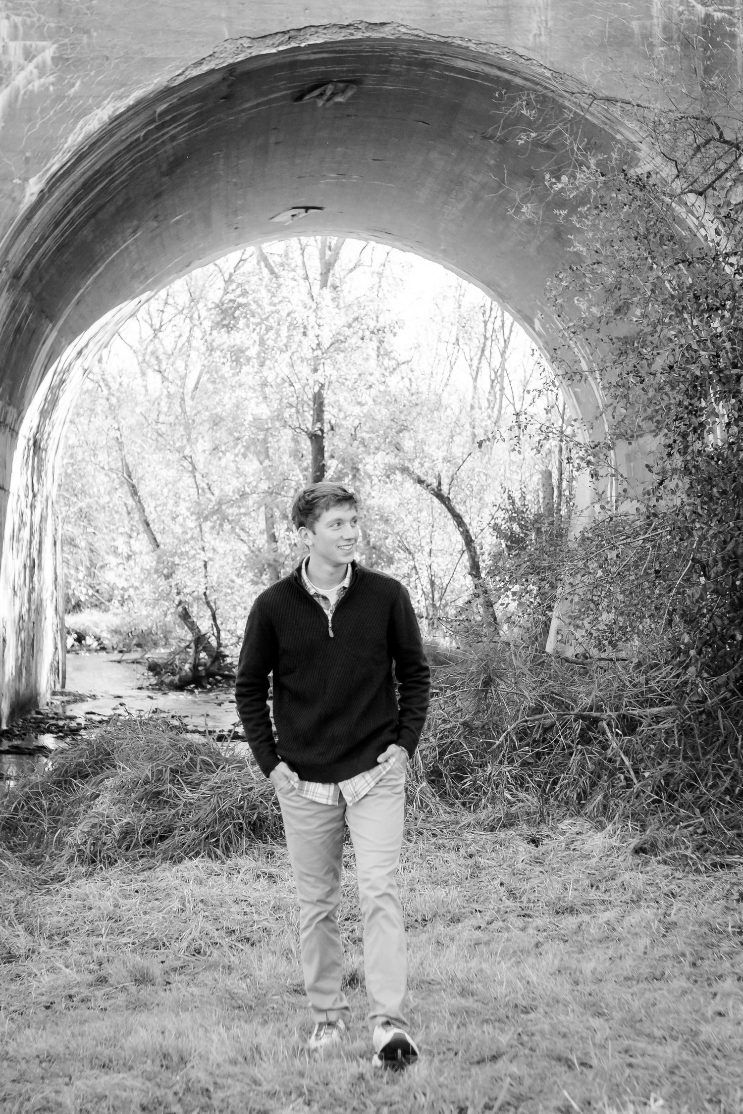 A series of black and white photos showing a person walking under a stone bridge archway in a natural setting during his Hartland session