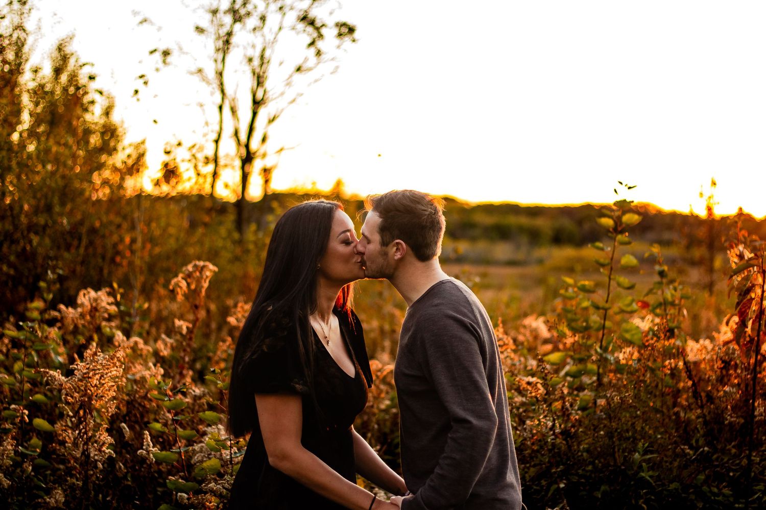 A romantic sunset moment captured in golden light among wildflowers and tall grass.