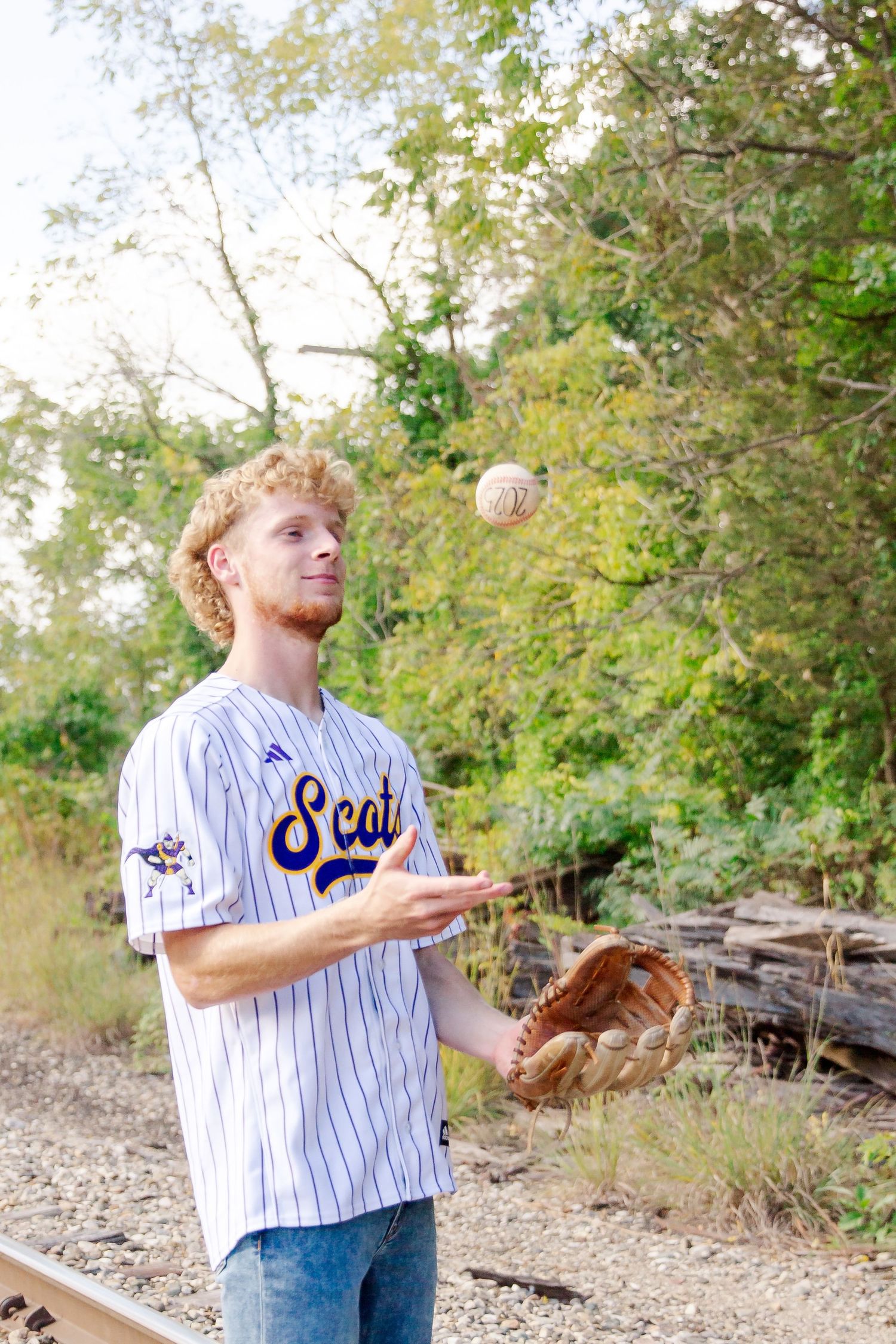 Baseball player in pinstriped jersey practices catching with a baseball and glove in an outdoor setting during a Michigan senior session