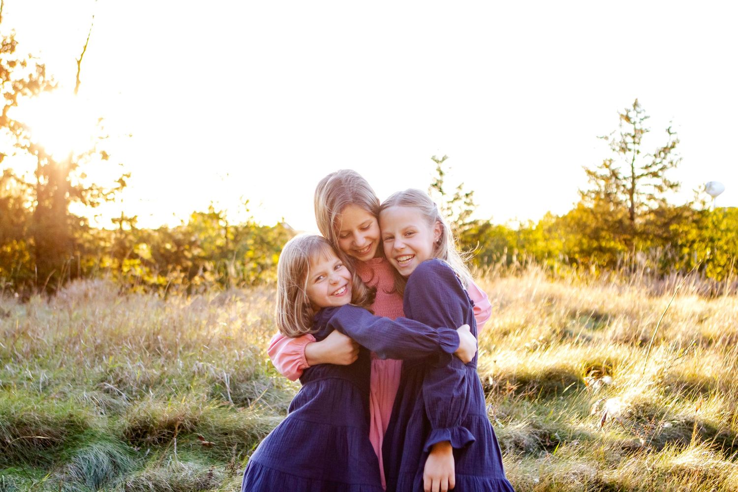 A family shares joyful embraces in a golden sunlit field during sunset at an Oconomowoc family session